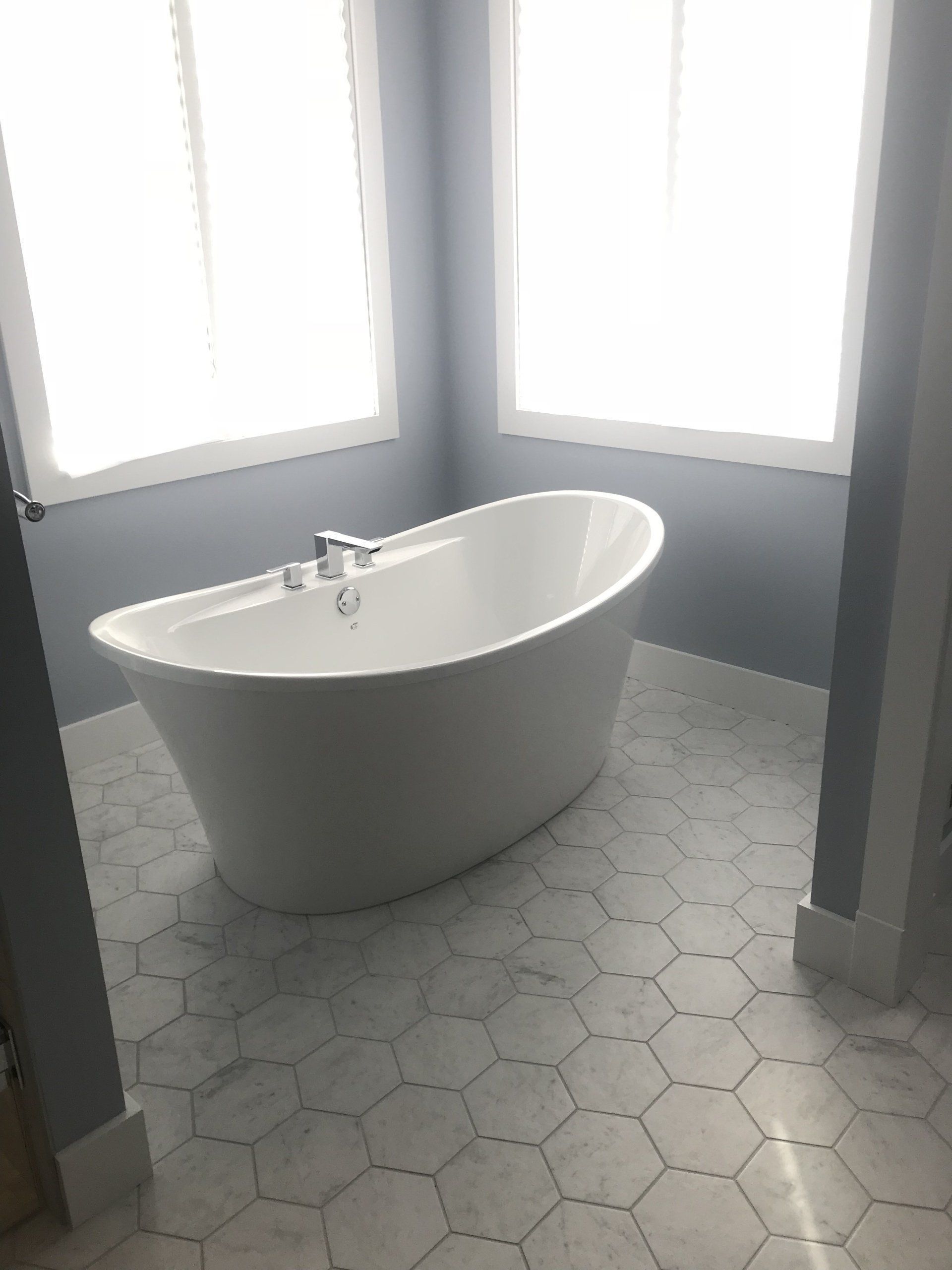 Modern bathroom with a freestanding white bathtub on gray hex tile floor by bright windows