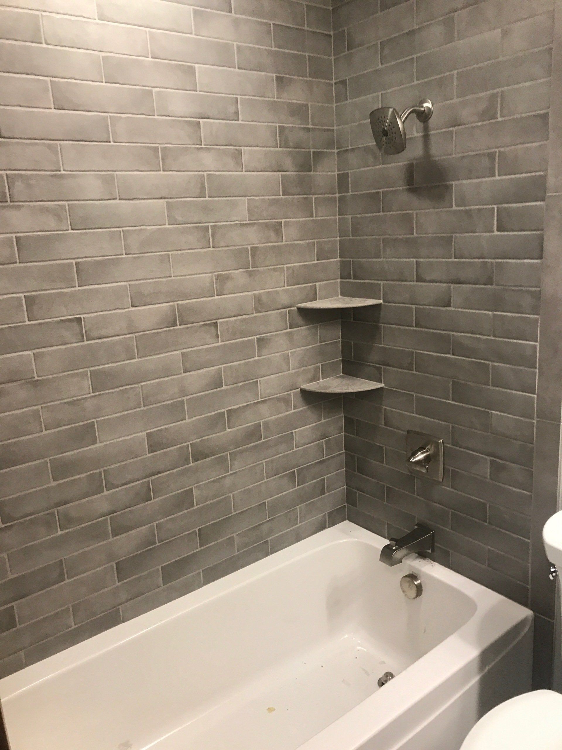 Gray-tiled shower with white bathtub, corner shelves, and chrome shower fixtures
