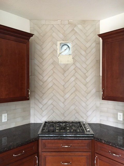 Kitchen with dark wood cabinets, black countertops, and a gas cooktop against a tiled herringbone backsplash.