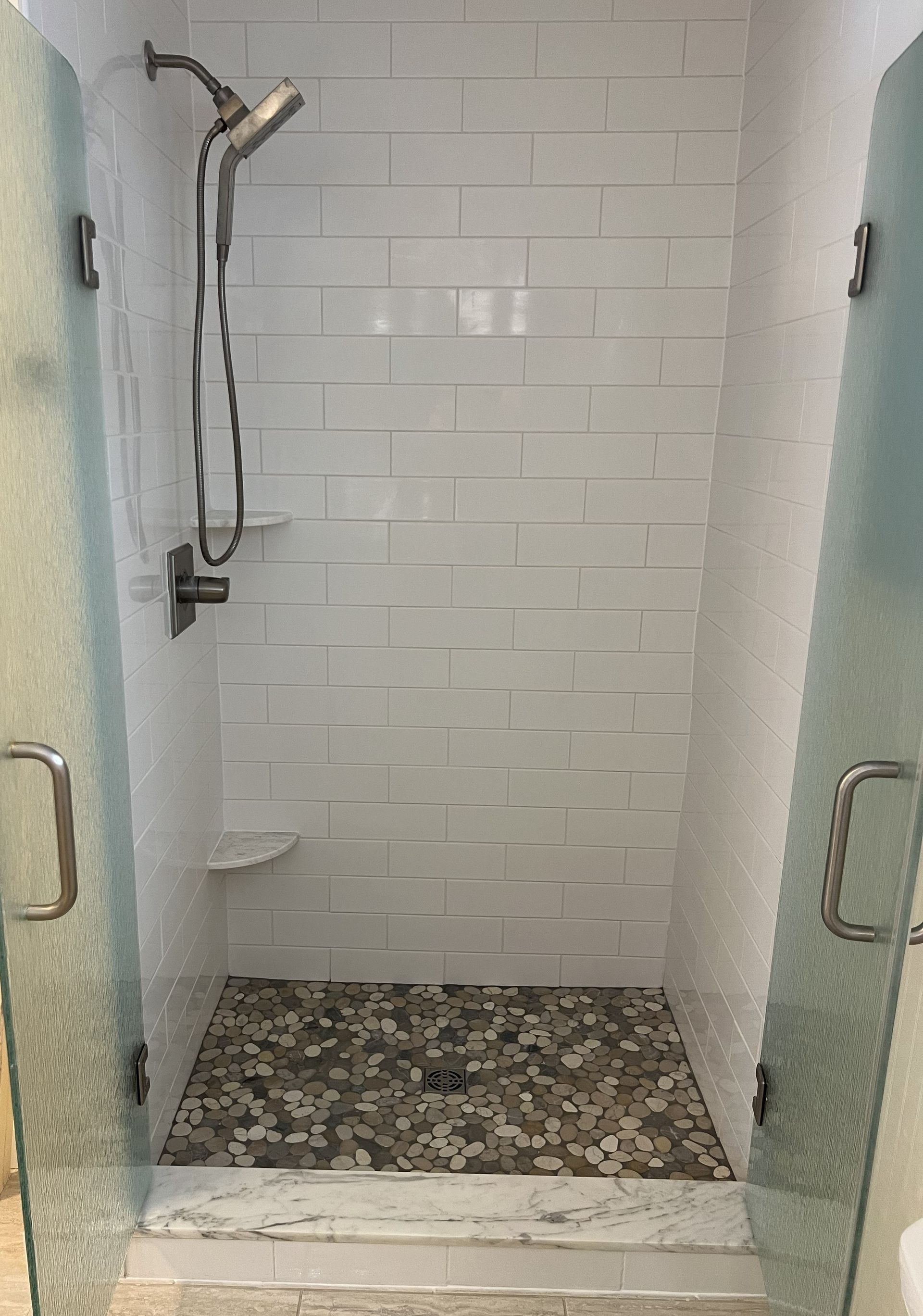 Small tiled shower stall with frosted glass doors, handheld showerhead, and pebble floor.