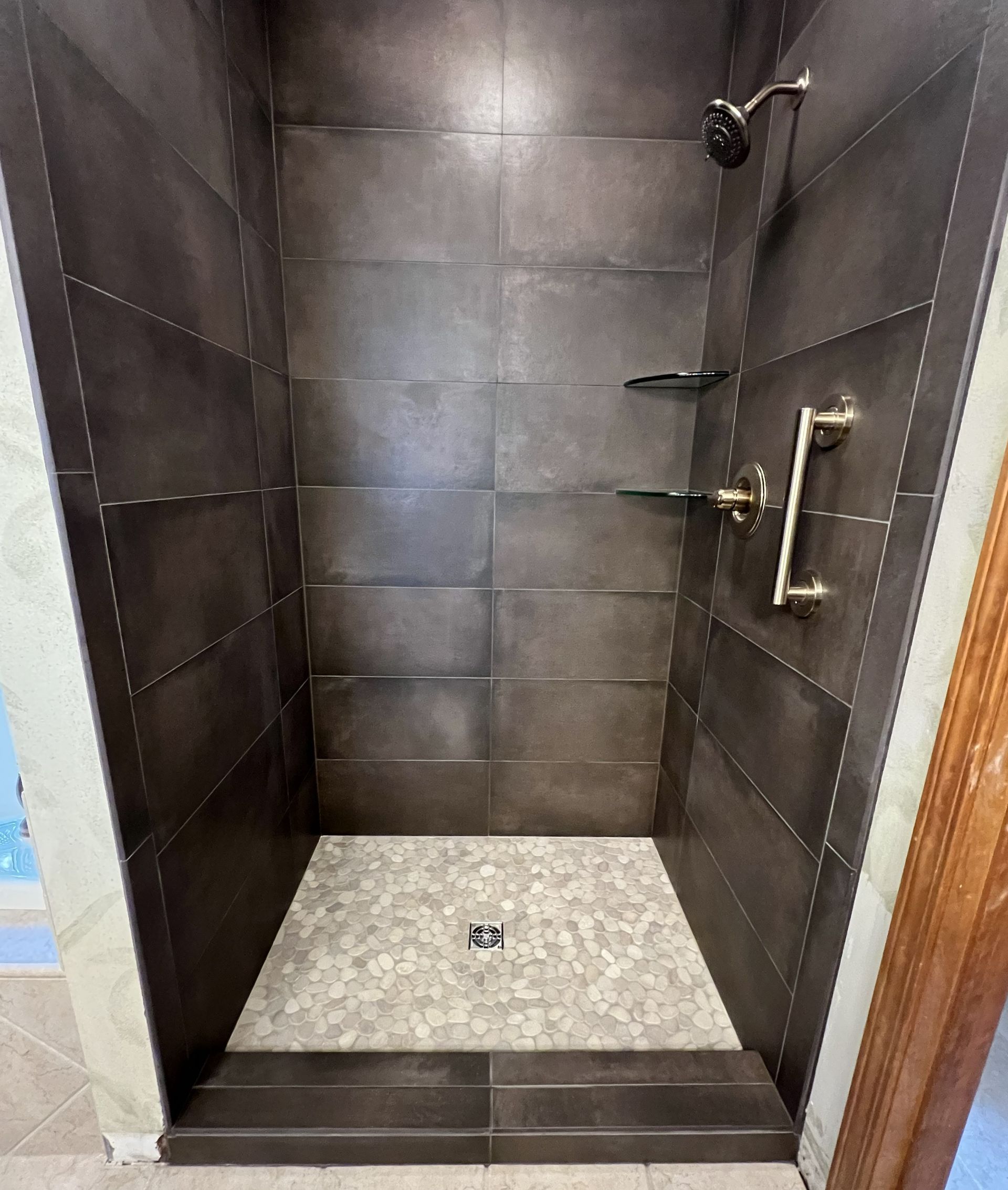 Empty walk-in shower with dark tile walls, light floor, and glass entry edge visible
