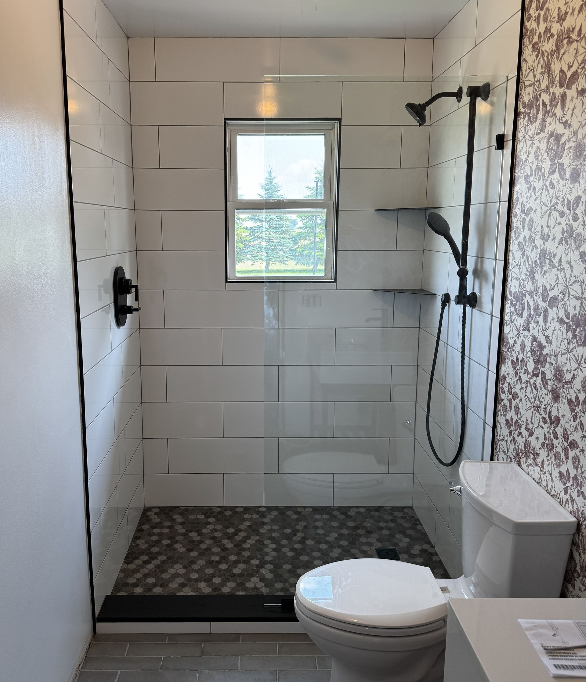 Small tiled bathroom with a walk-in shower, toilet, and window.
