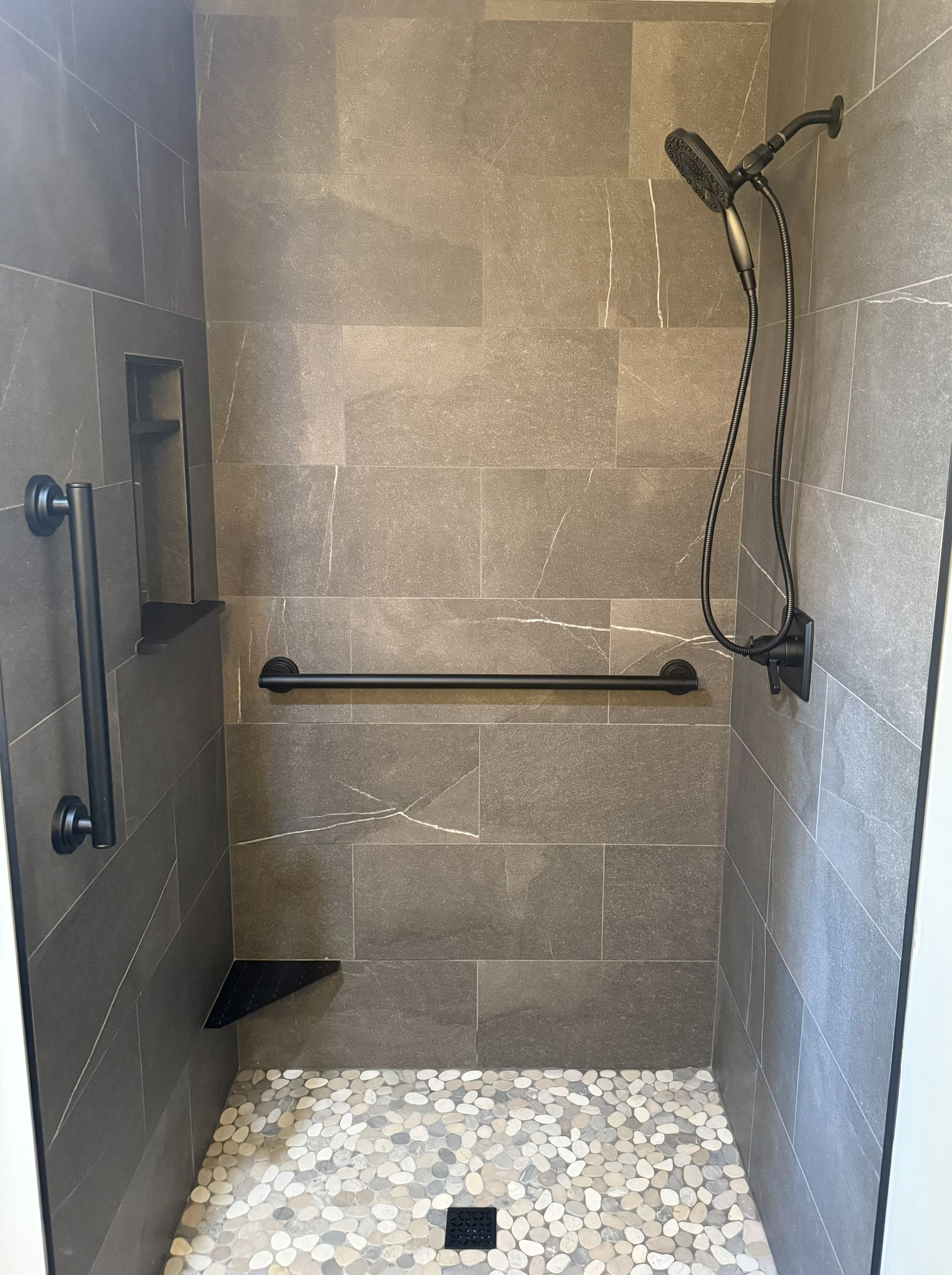 Accessible shower stall with grab bars, handheld showerhead, and tiled floor.