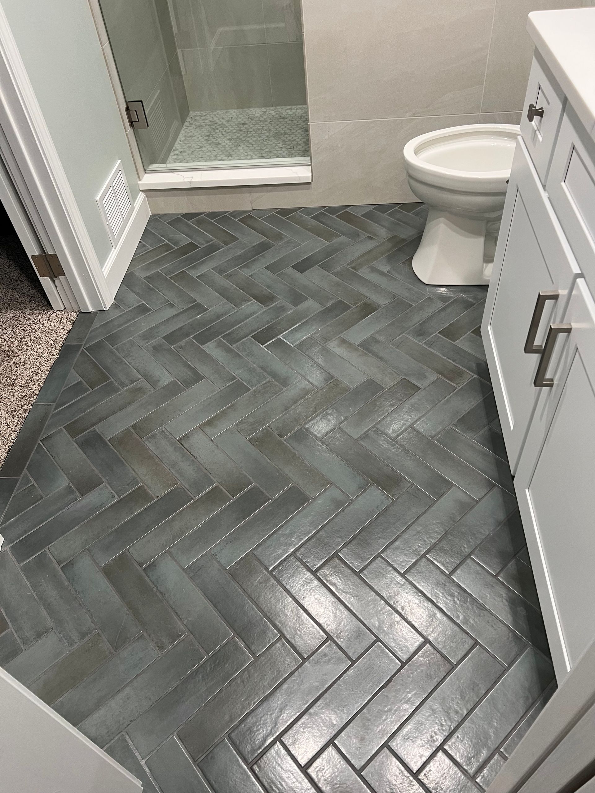 Dark herringbone tile bathroom floor with white vanity, toilet, and shower stall