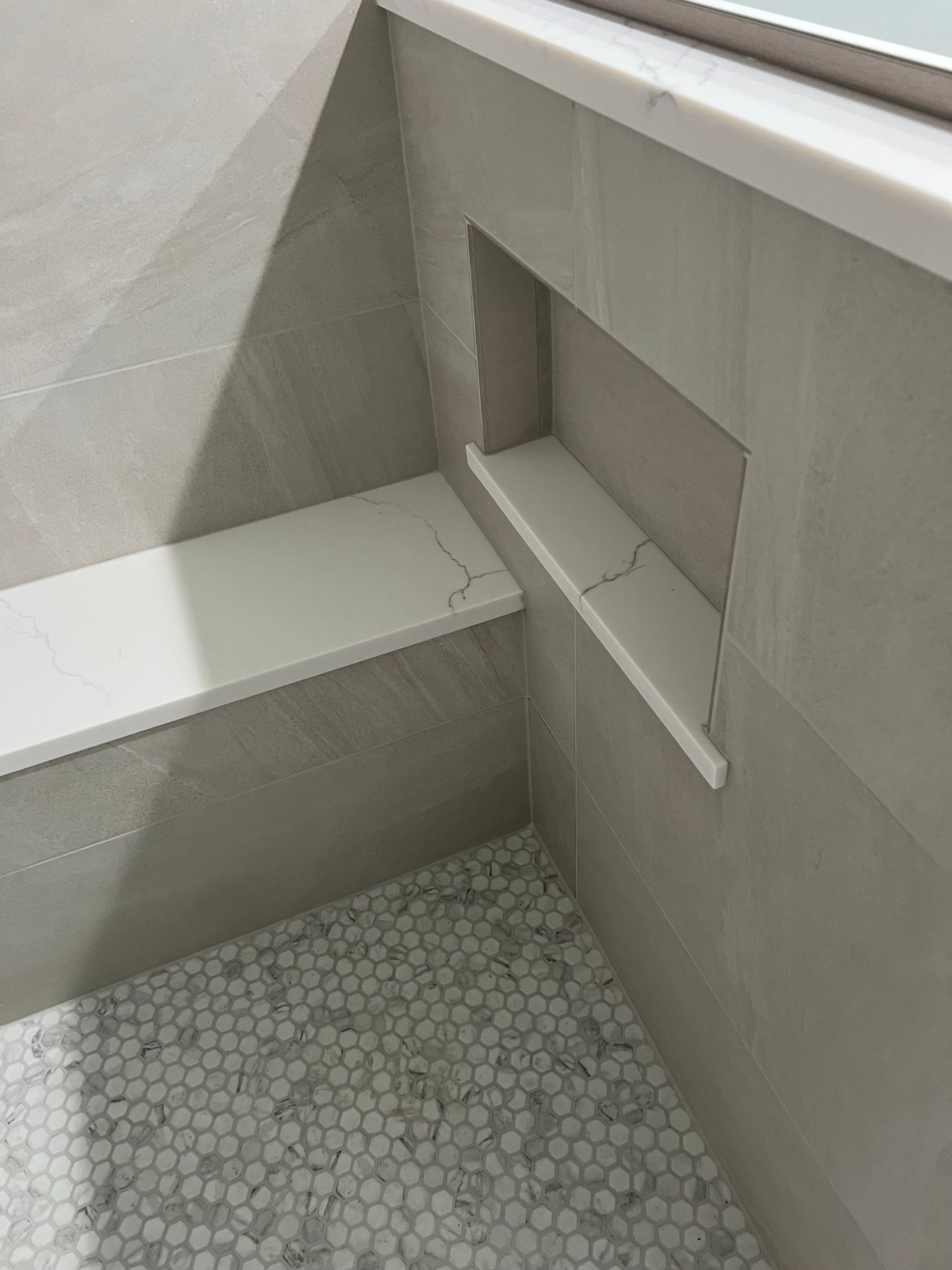 Small tiled bathroom corner with a built-in bench and recessed shelf beside a bathtub.