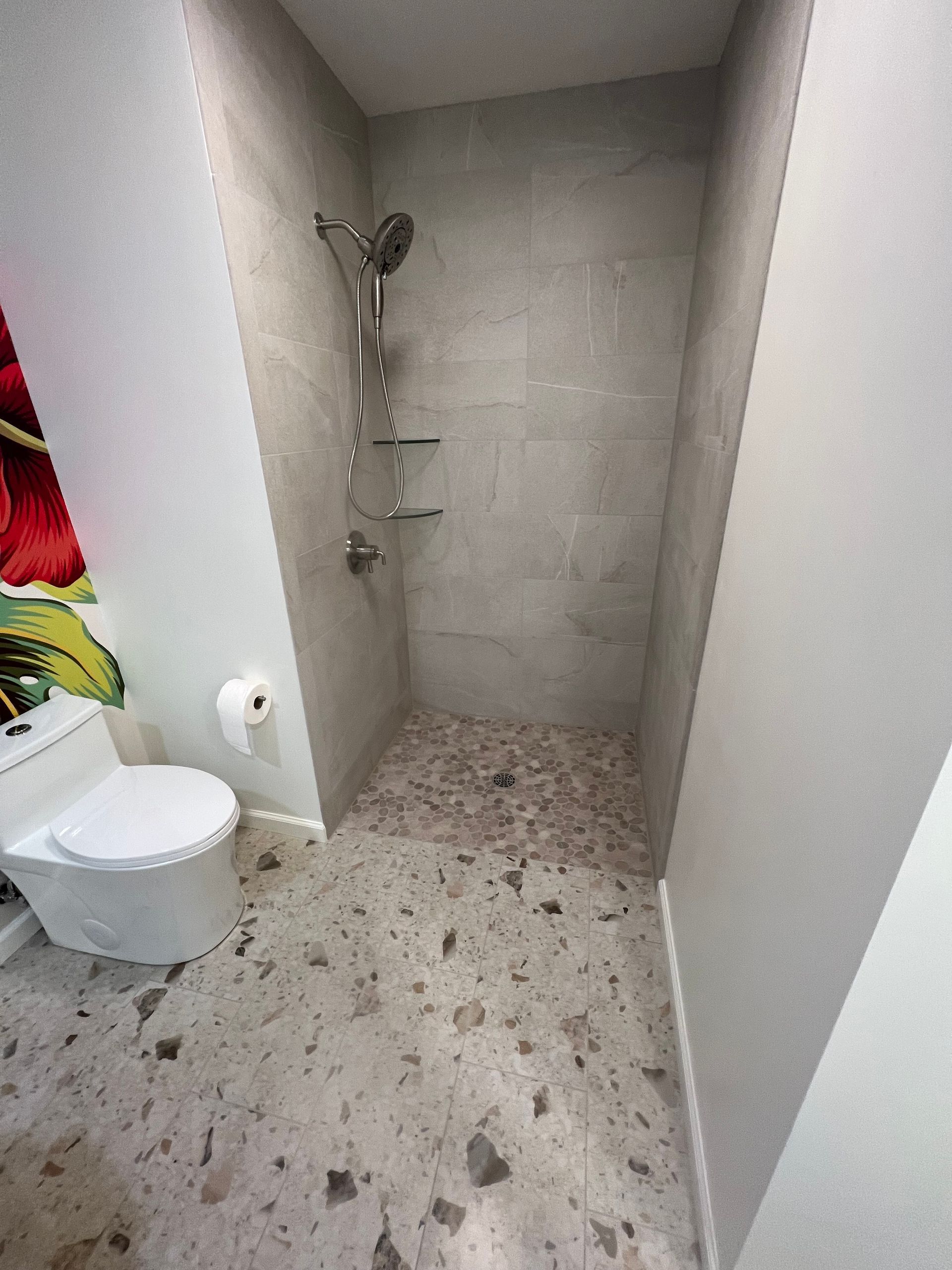 Small bathroom with a toilet and walk-in shower, light tile walls, and speckled floor.