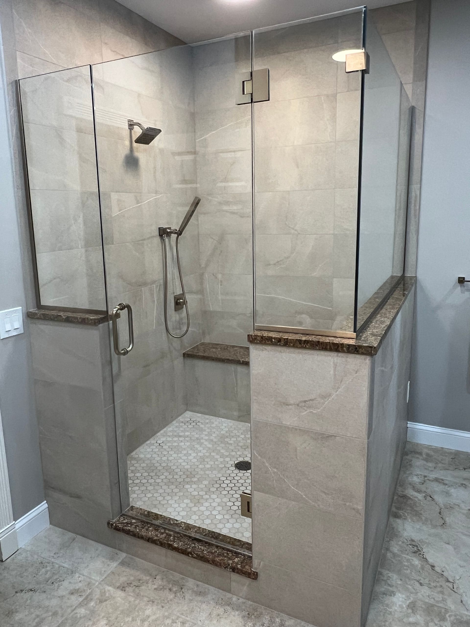 Glass-enclosed tiled shower with handheld sprayer, built-in bench, and pebble floor.