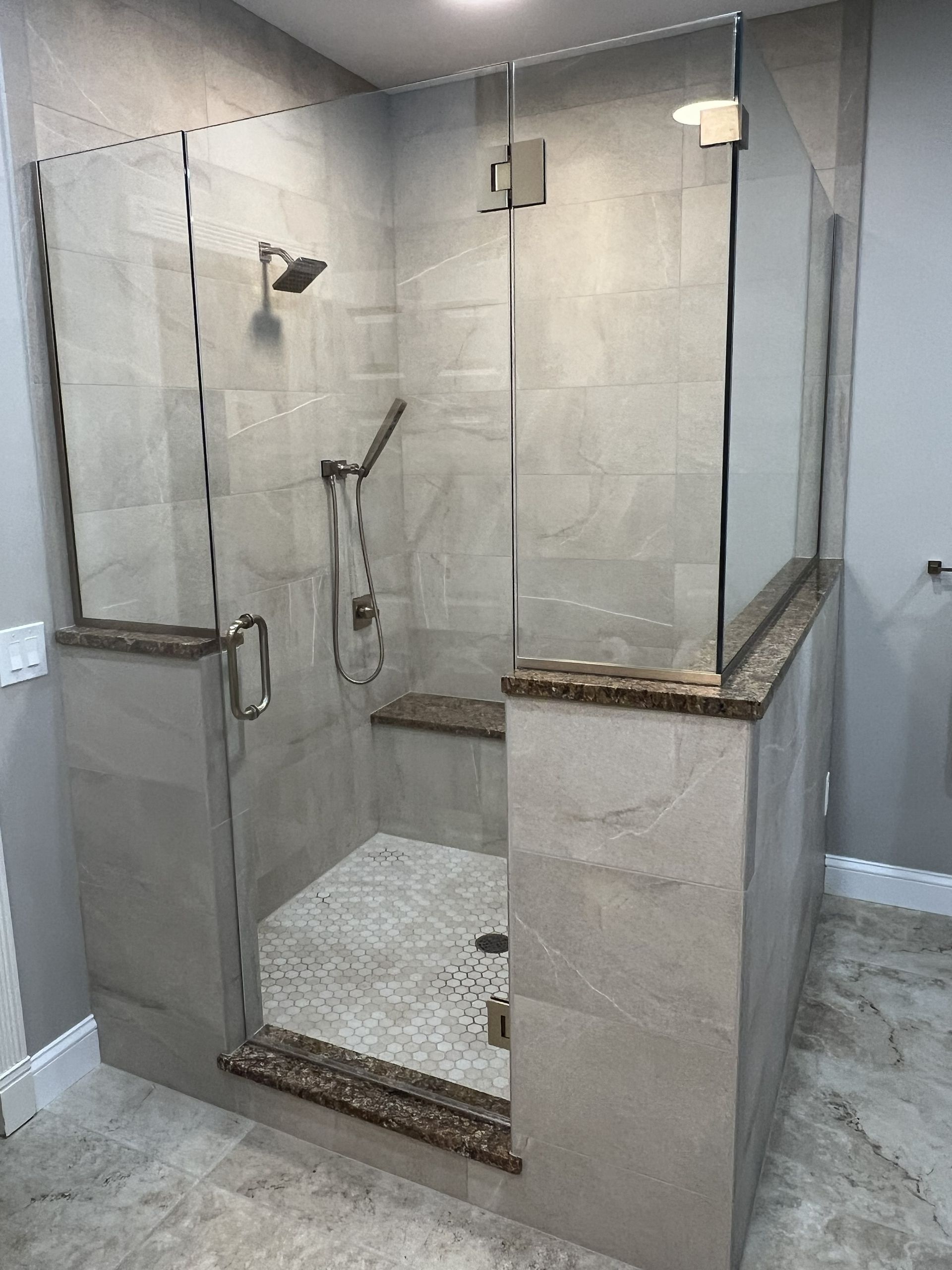 Modern walk-in shower with glass enclosure, gray tile walls, and mosaic pebble floor.
