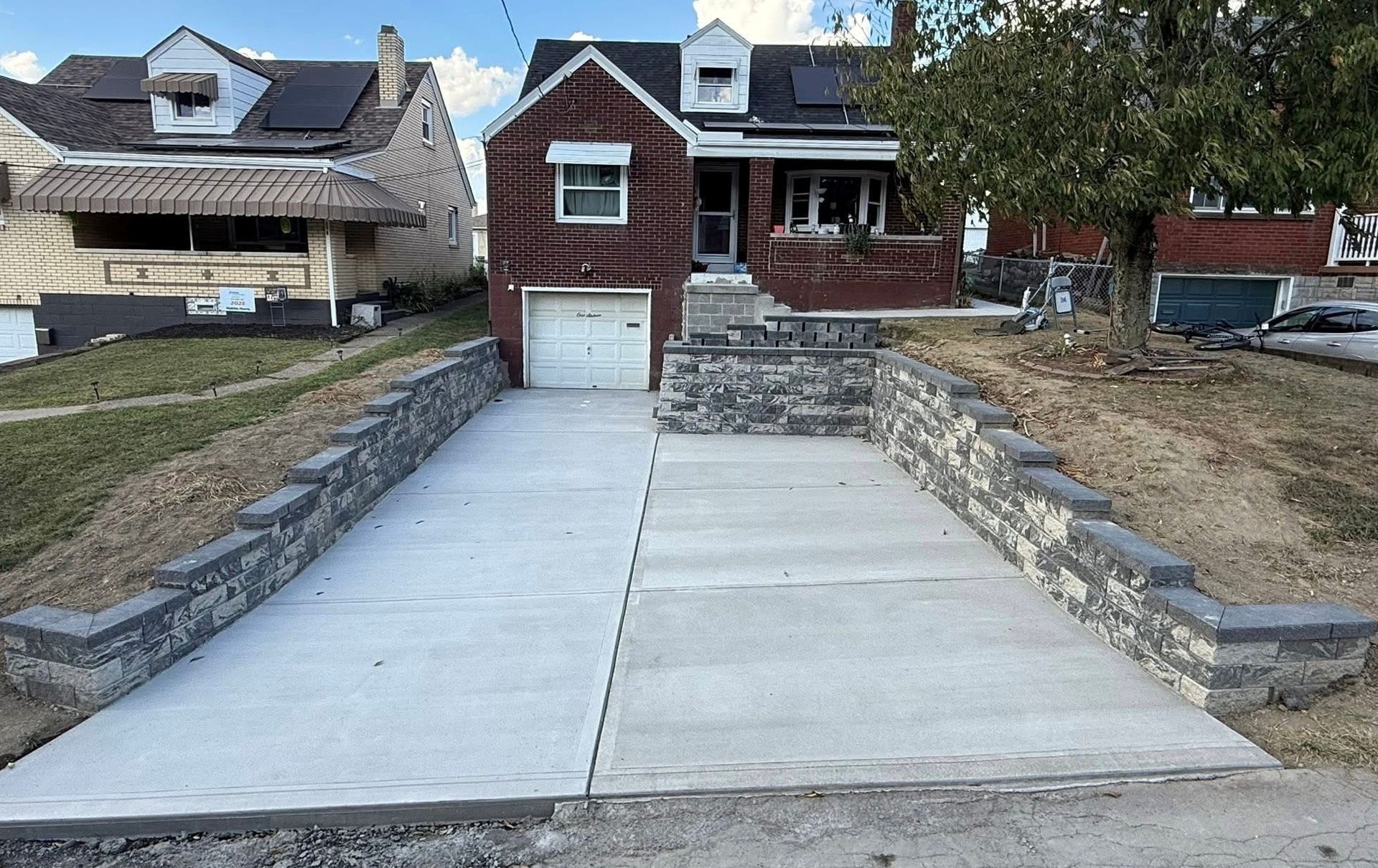 Concrete driveway leading to a brick house with stone retaining walls and a front porch