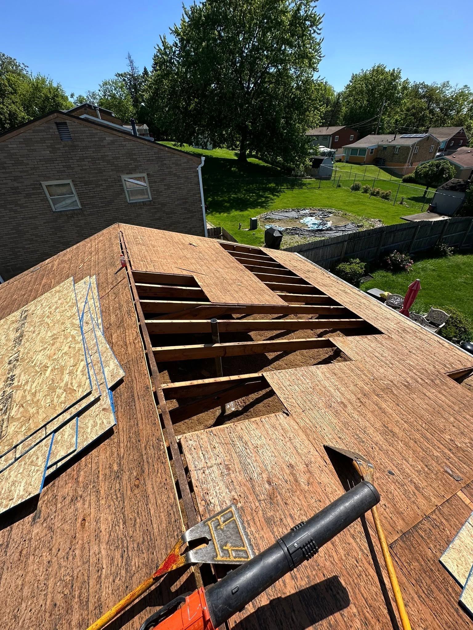 Roof under repair with exposed wooden framing and shingles, overlooking a grassy residential yard.