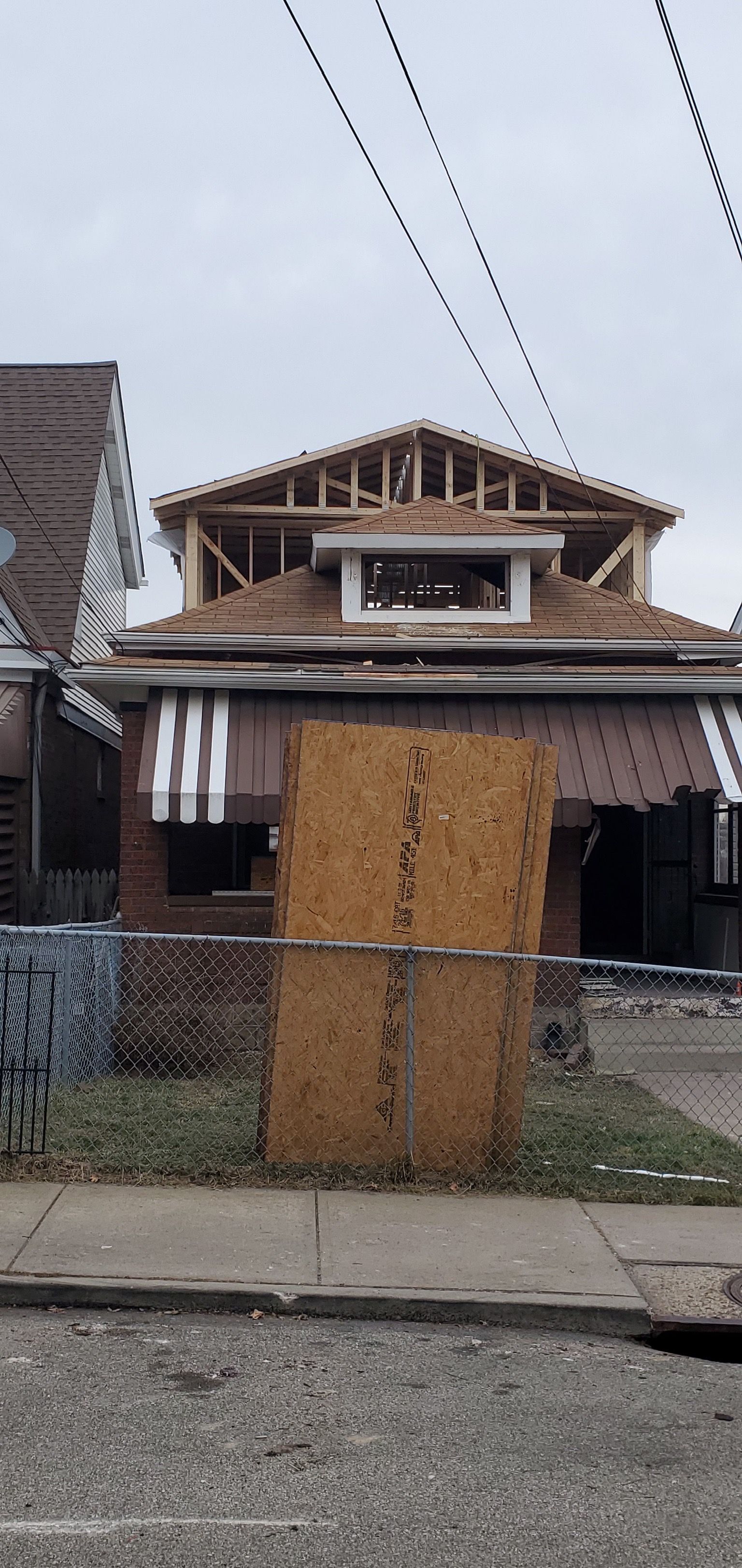 Boarded-up house with plywood over the front door and windows, power lines overhead, on a residential street.