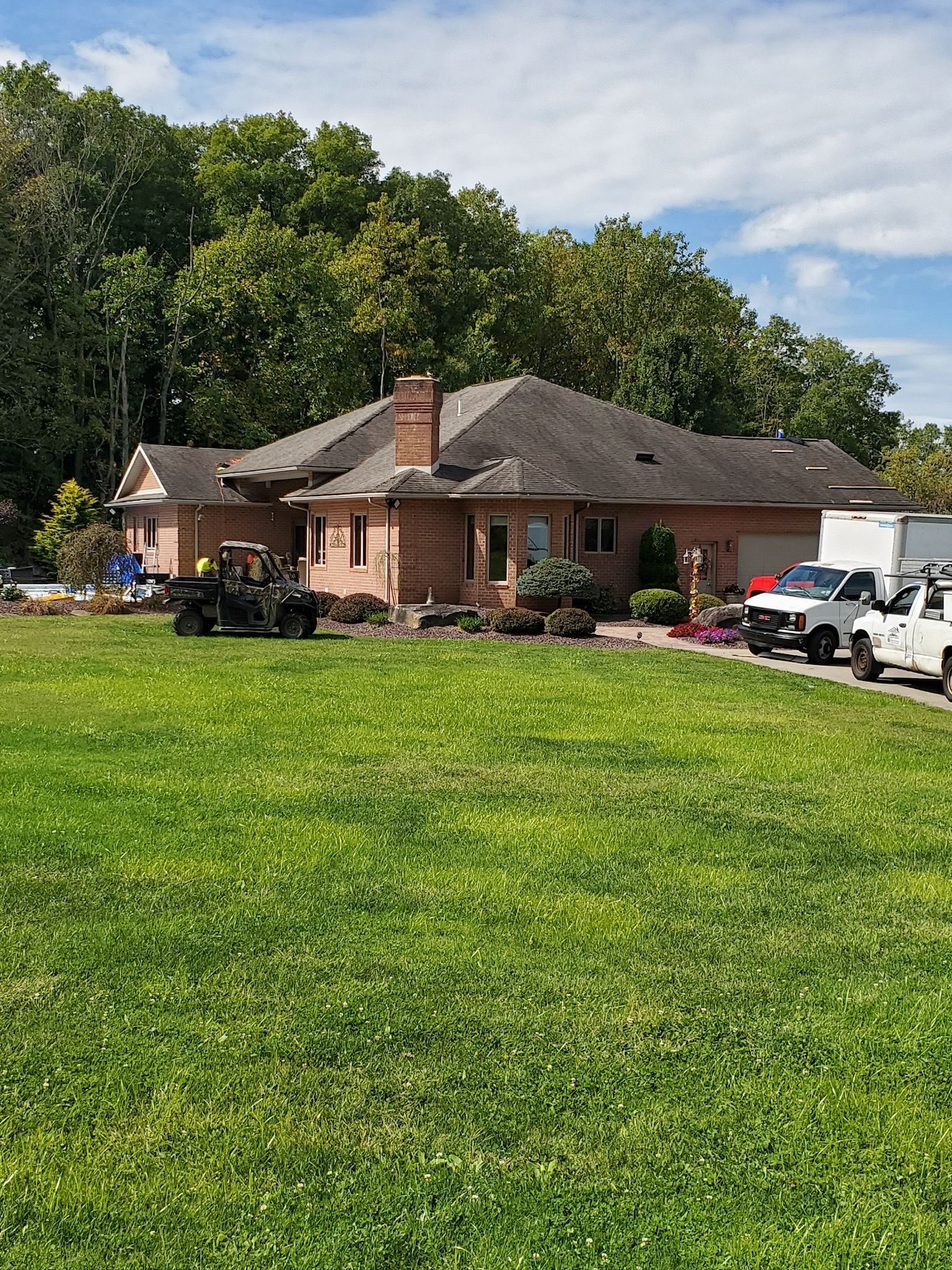 Brick house with a chimney, green lawn, trees, and parked vehicles in front