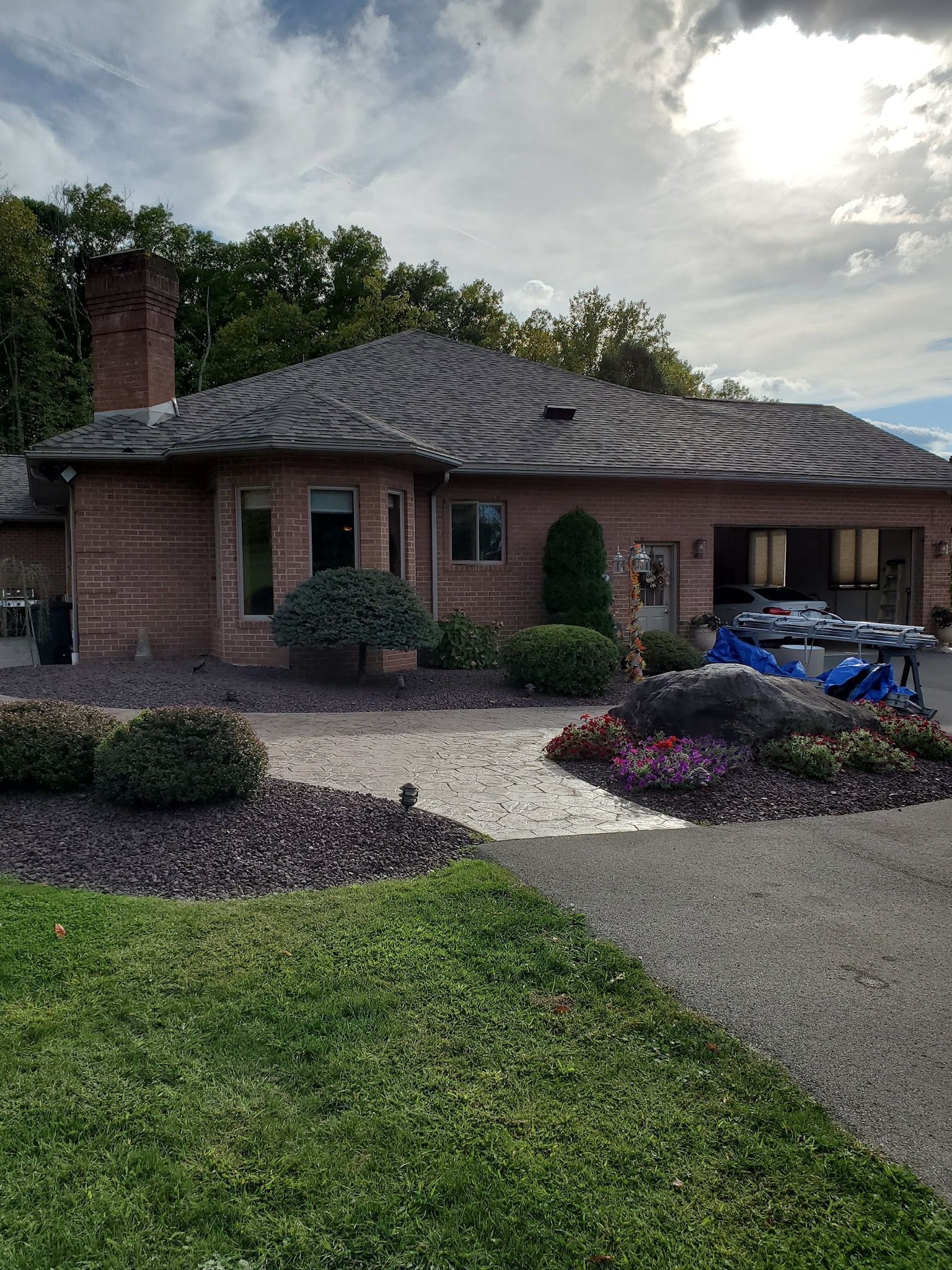 Brick house with dark roof, landscaped front yard, and a blue car parked in the driveway.