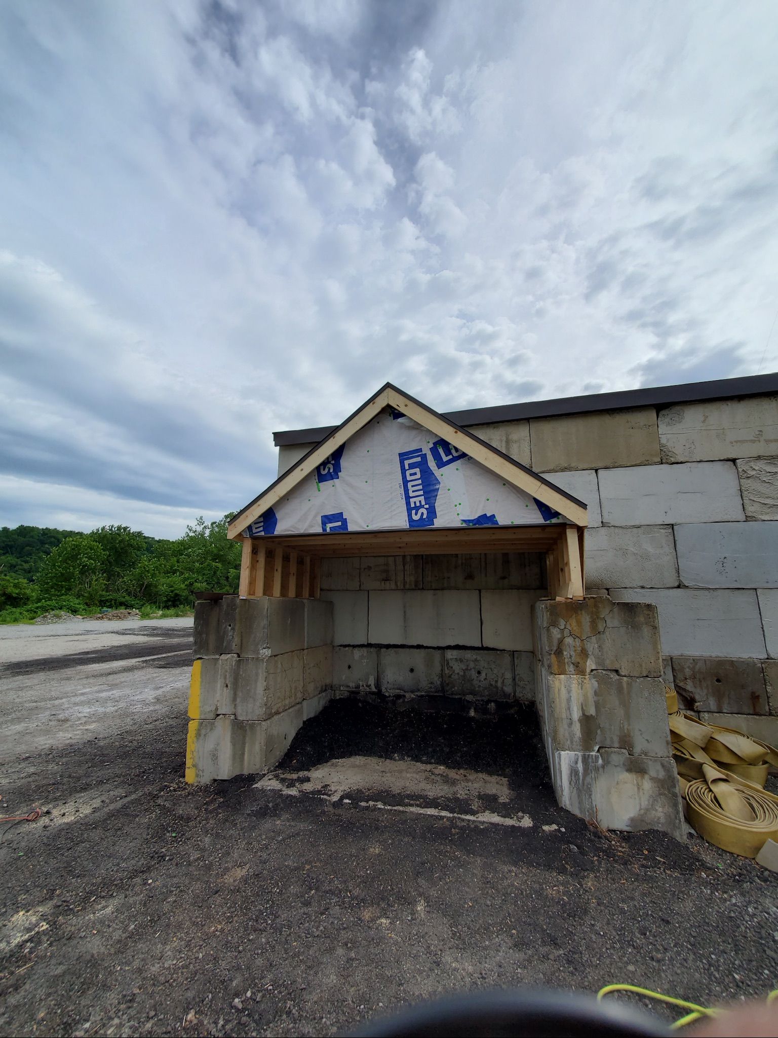Small stone shelter with a peaked roof and blue signs, set on a gravel lot under a cloudy sky.
