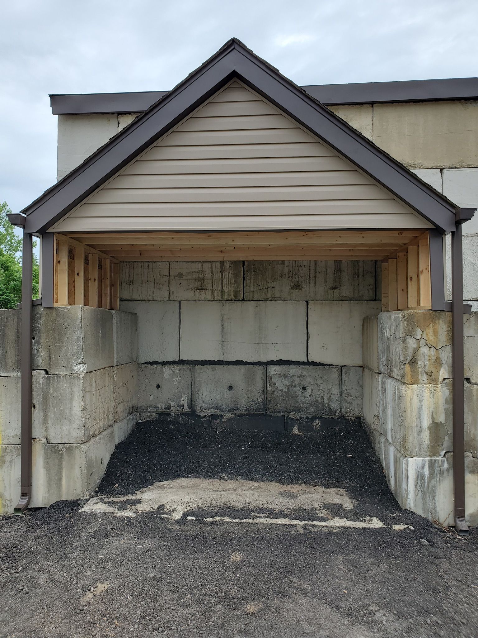 Open garage with cinder block walls, beige siding, and gravel floor.