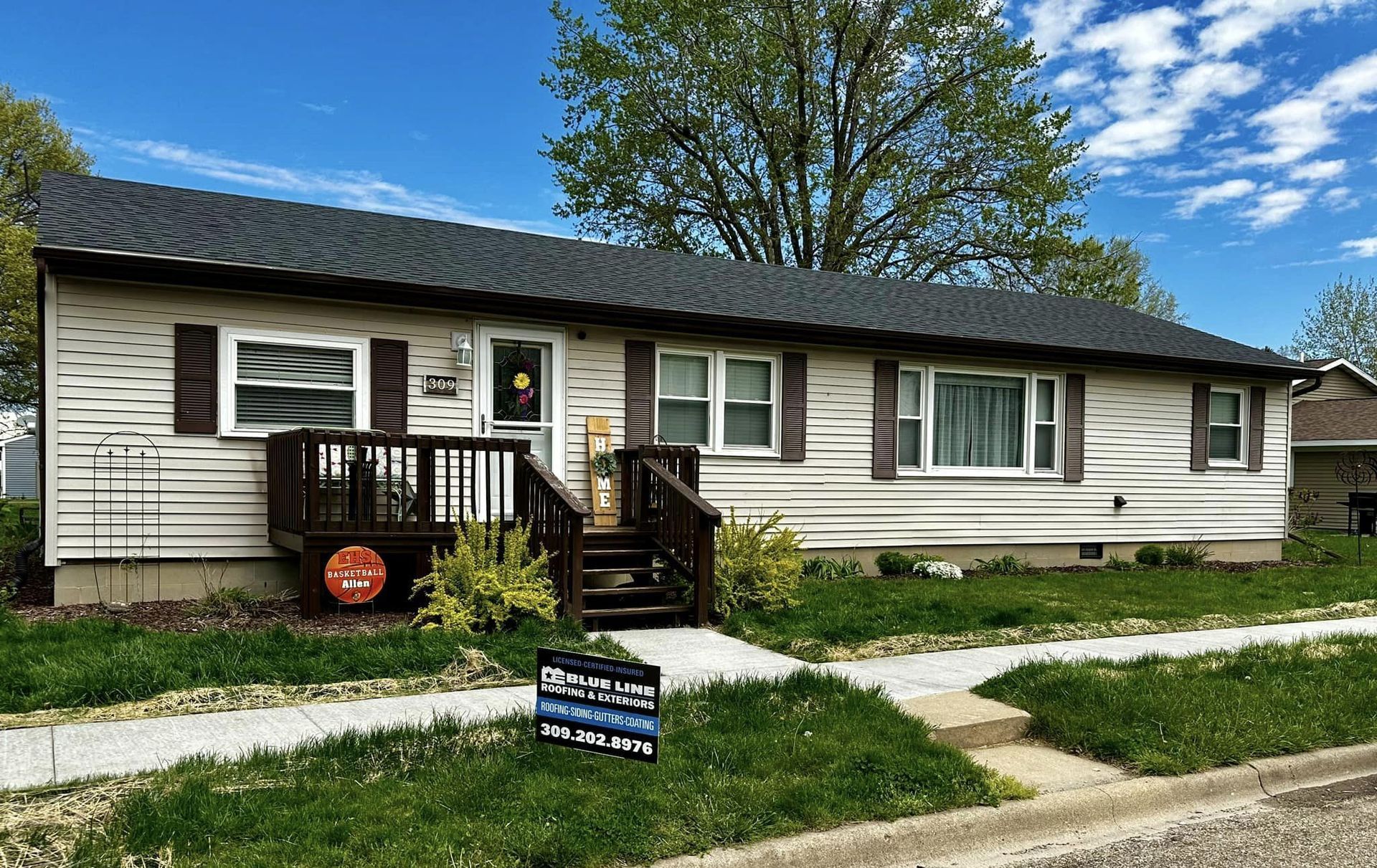 A white house with a black roof and a sign in front of it.