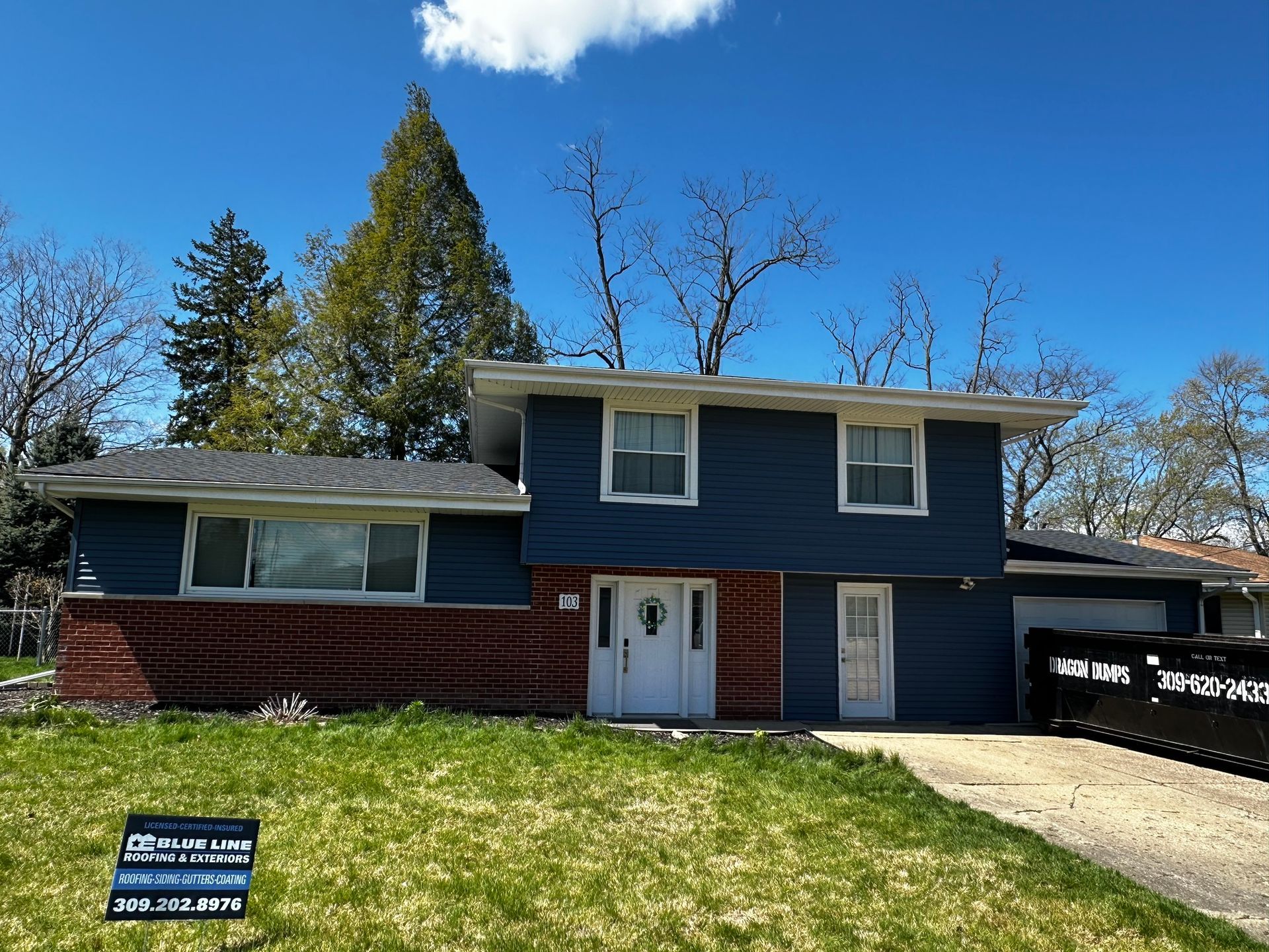 A house with a blue siding and a sign in front of it.