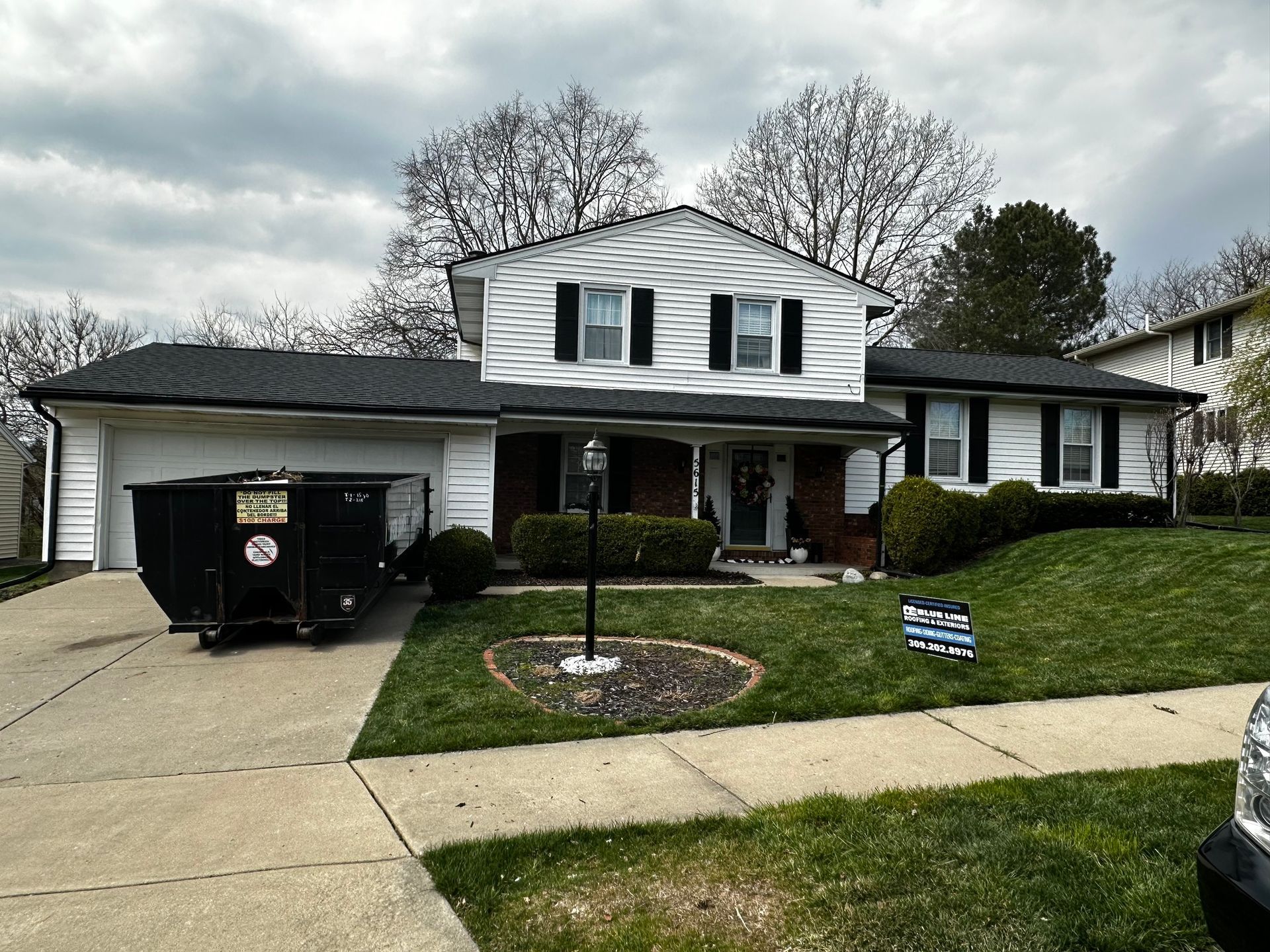 A large white house with a black dumpster parked in front of it.