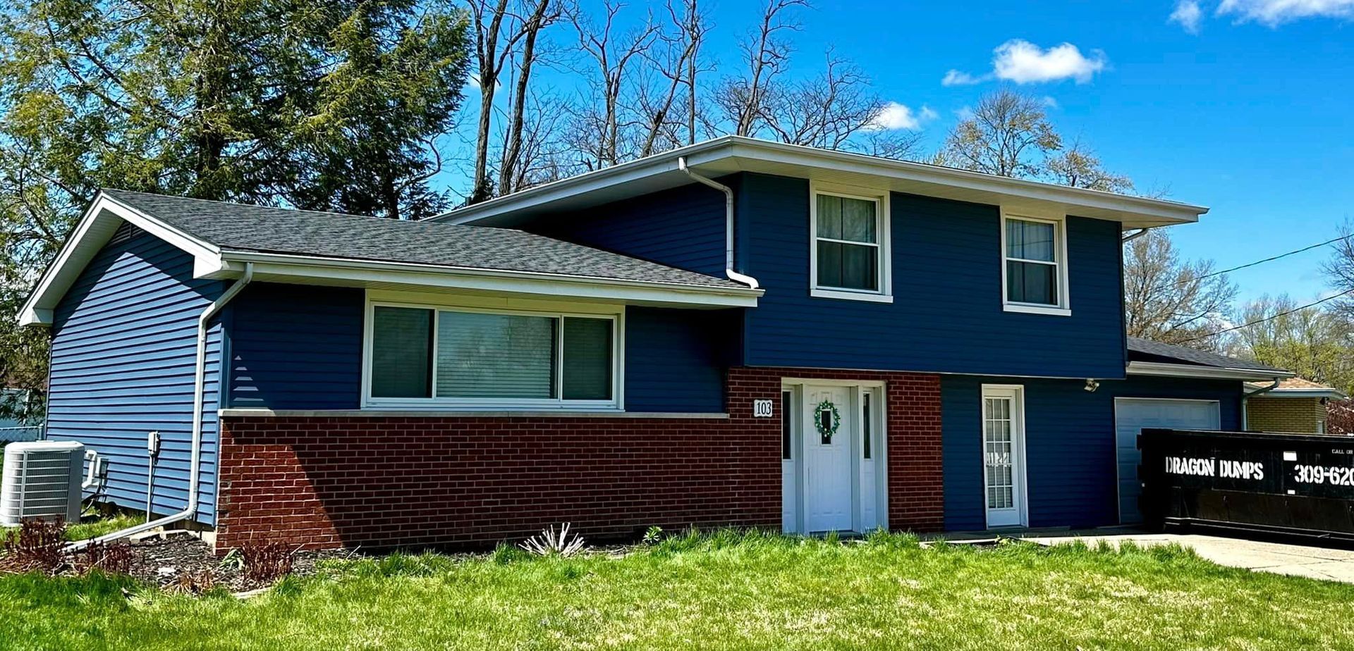 A blue house with a red brick foundation is sitting on top of a lush green lawn.