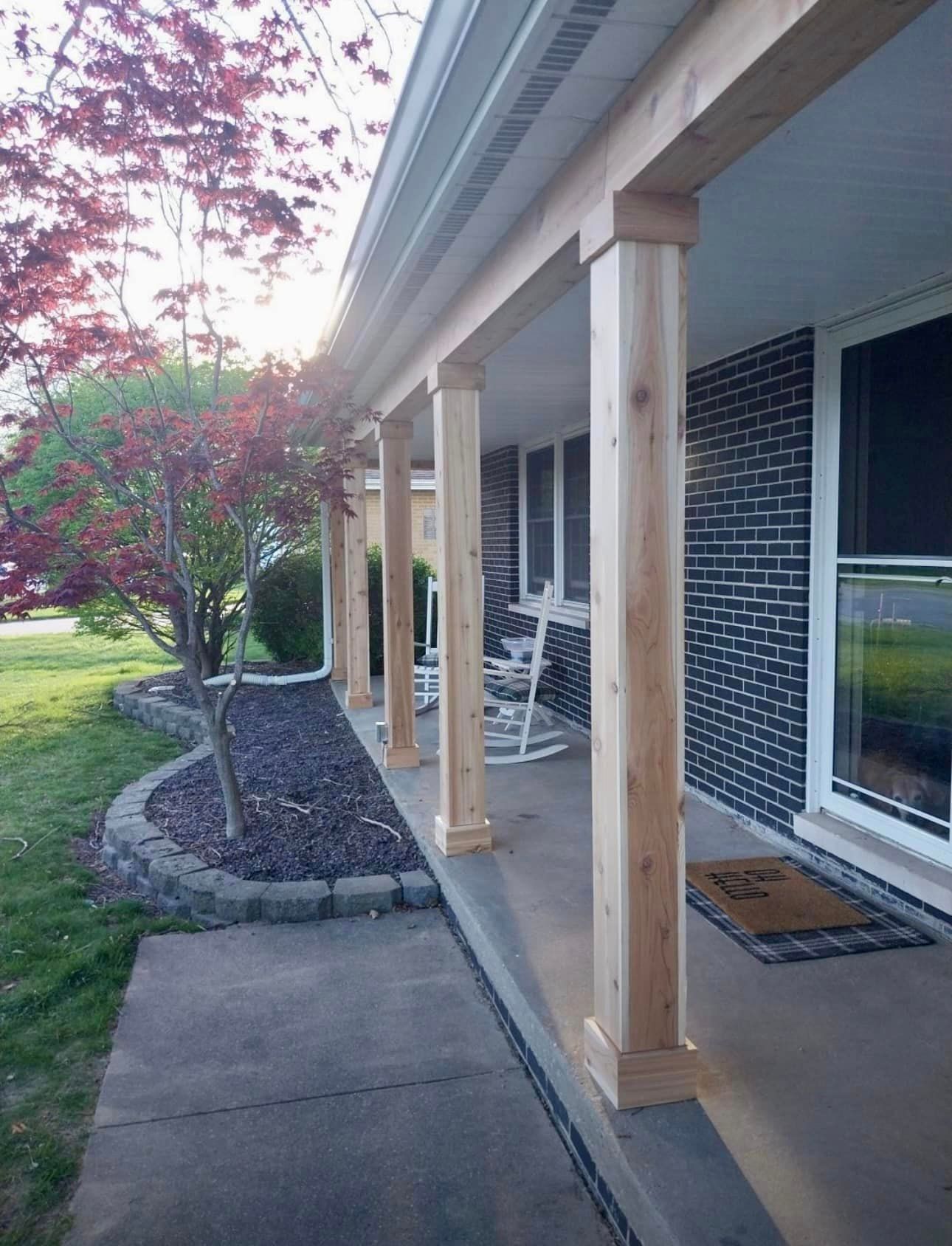A porch with wooden pillars and rocking chairs on it.