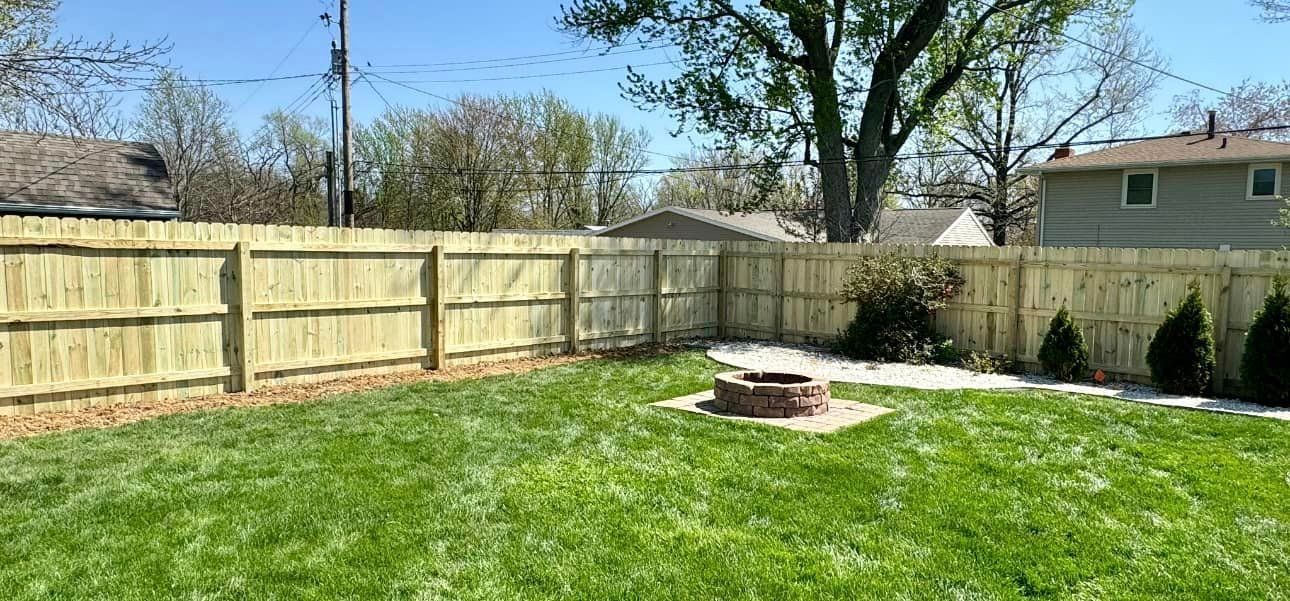 A backyard with a wooden fence and a fire pit.