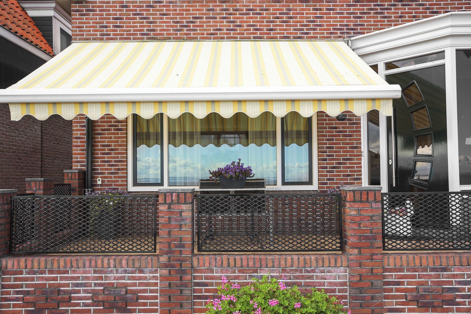 Brick building with awning over windows, black metal fence, and flower box with purple flowers.