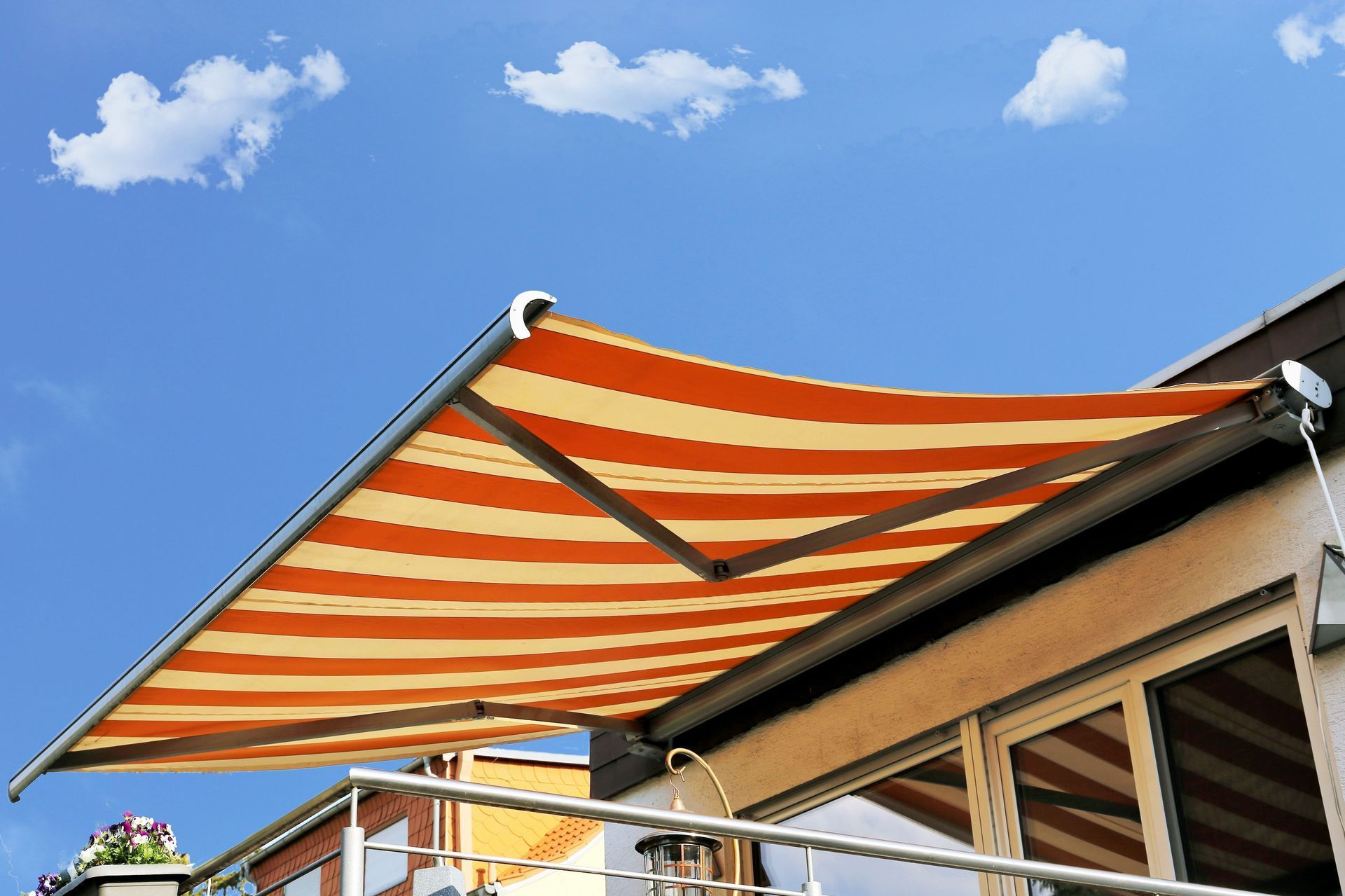 Orange and white striped awning extended from a balcony, under a blue sky with clouds.