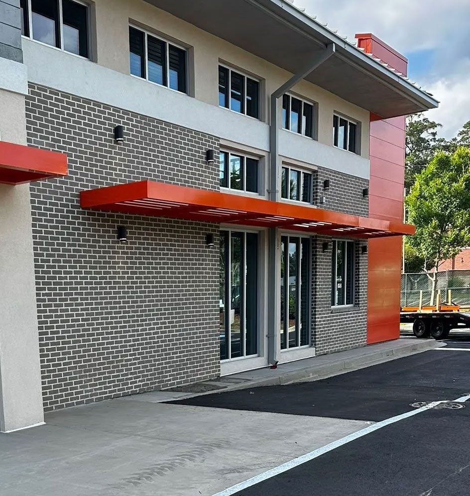 Building entrance with orange awnings, textured gray and beige walls, and a black asphalt surface.