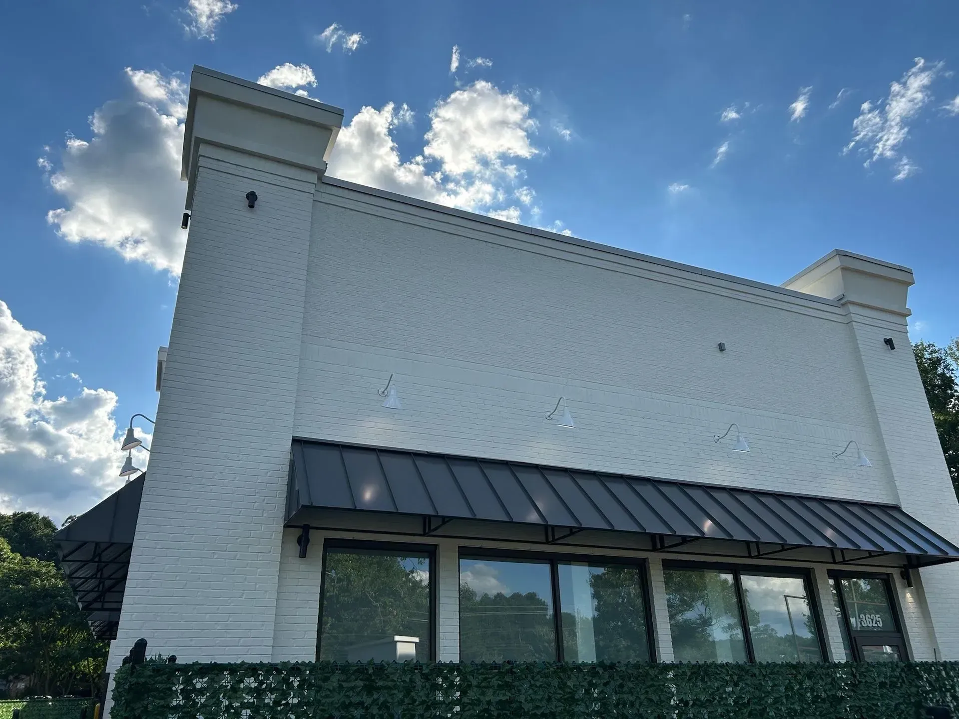 White brick building with black awning and large windows against a blue sky with clouds.