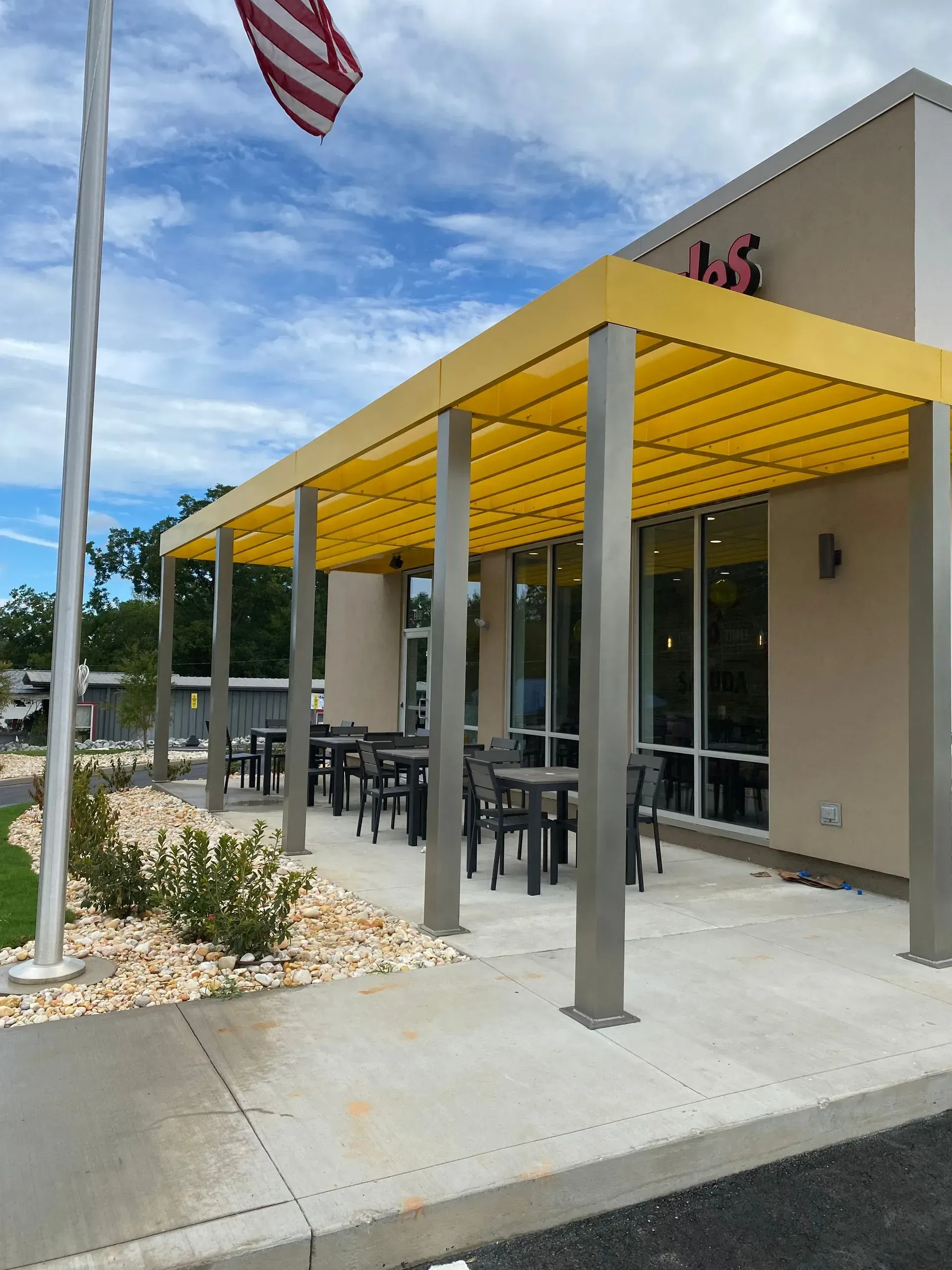 Outdoor seating area with yellow awning, tables, and chairs. Building with large windows. American flag flies.