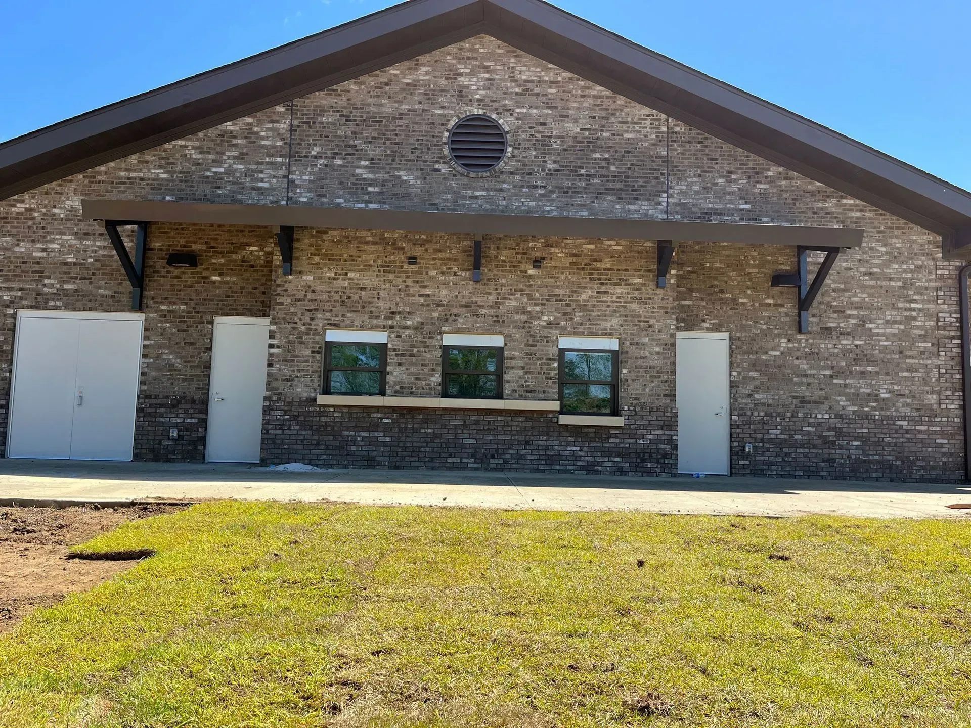 Brick building with awning, doors, and windows, set against a blue sky. Green grass in foreground.
