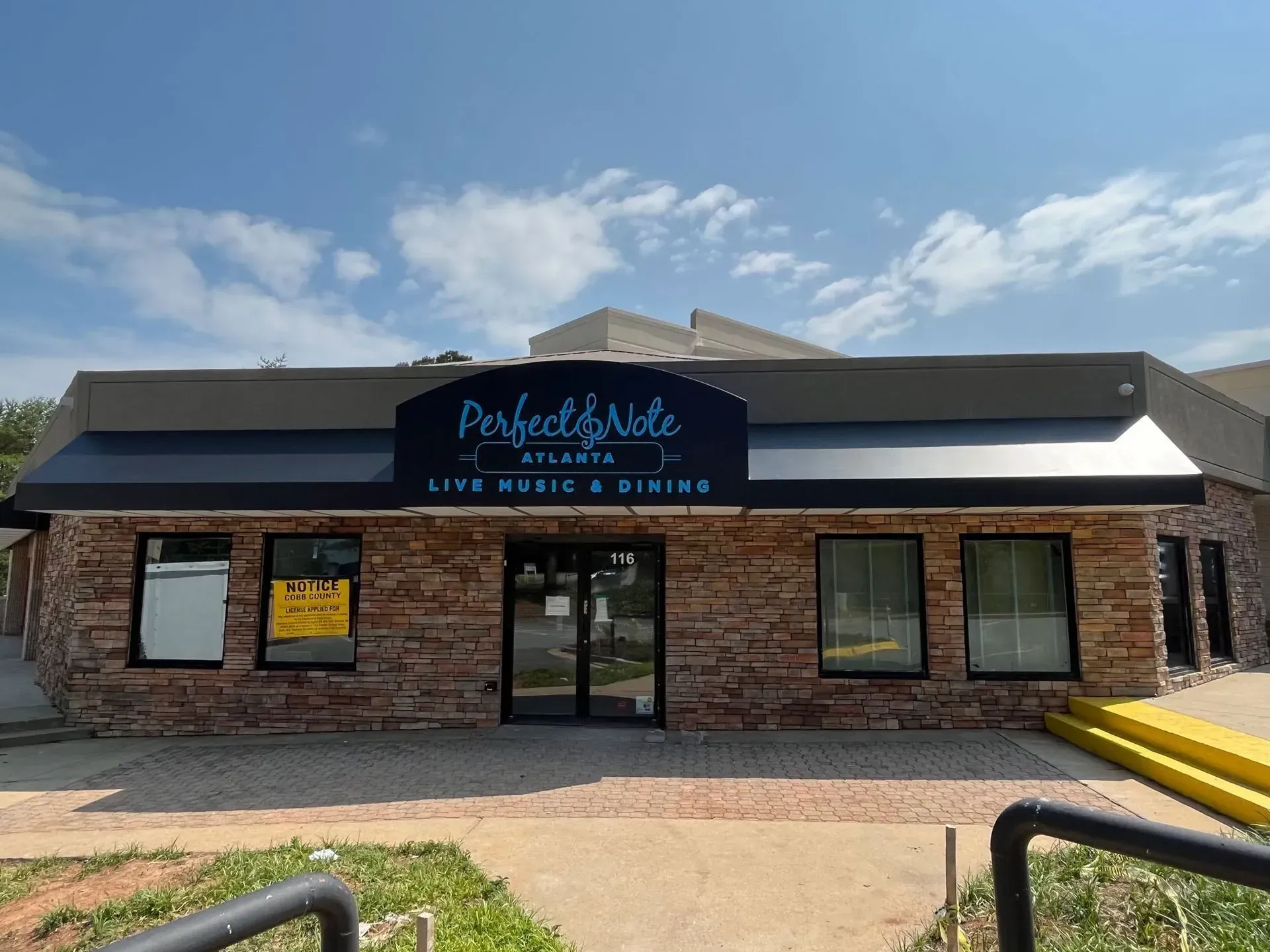 Exterior of "Perfect & Sete" cafe. Stone facade, black awning, glass doors, and sign with cafe, music & drinks text.