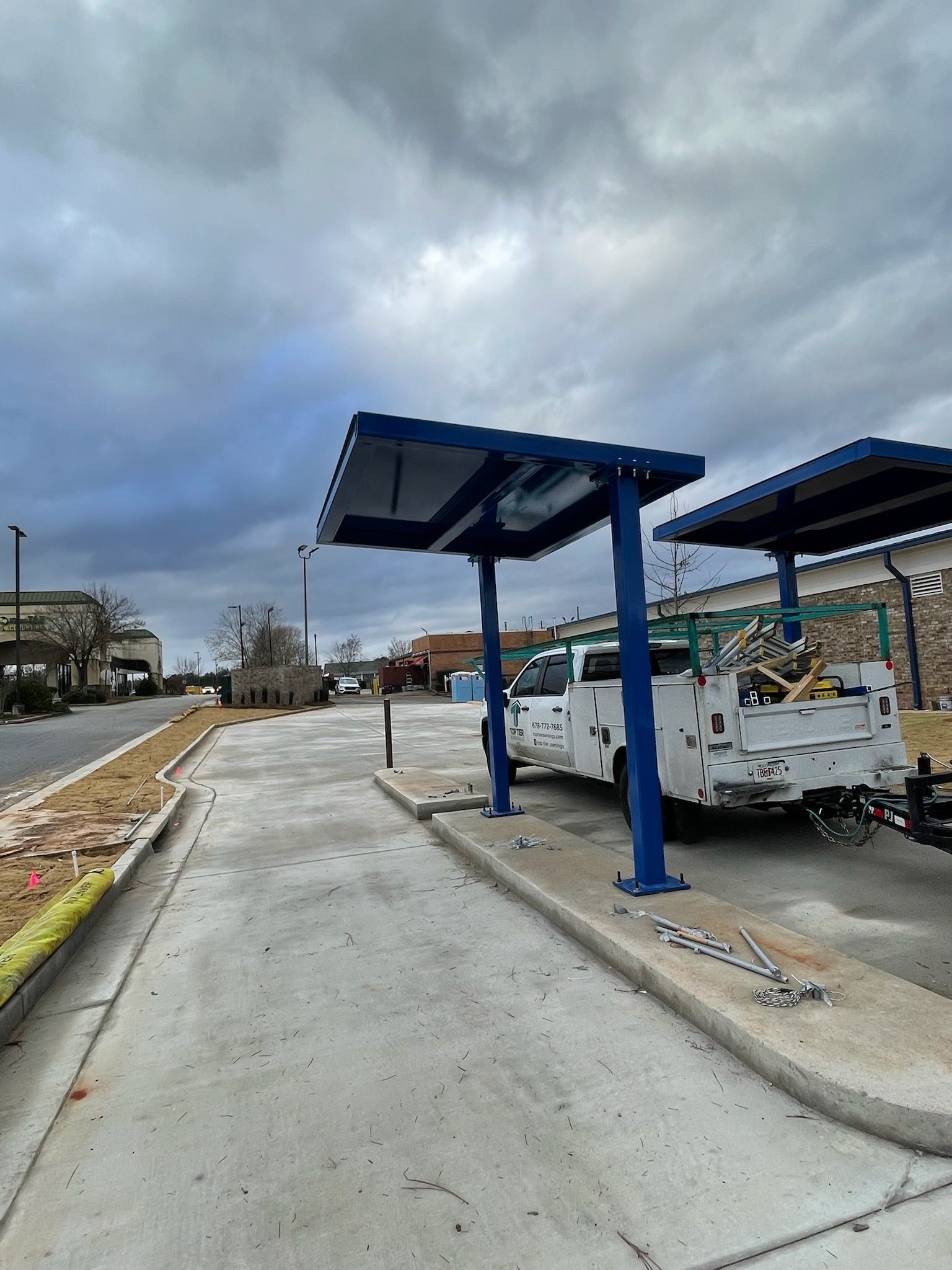 Blue-framed shelter structures with gray roofing in a concrete parking area under a cloudy sky.