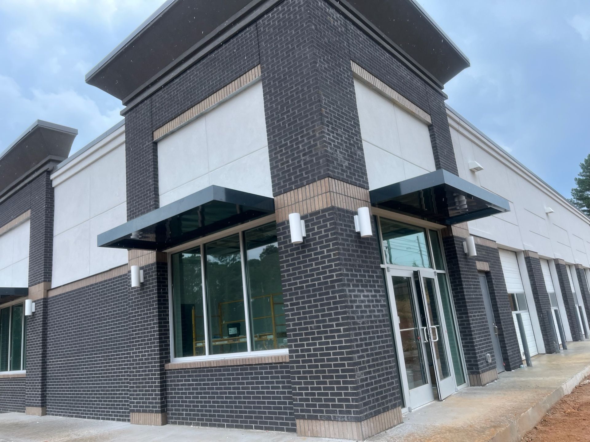 Exterior view of a commercial building with dark brick and gray awnings. Glass windows and a door are visible.