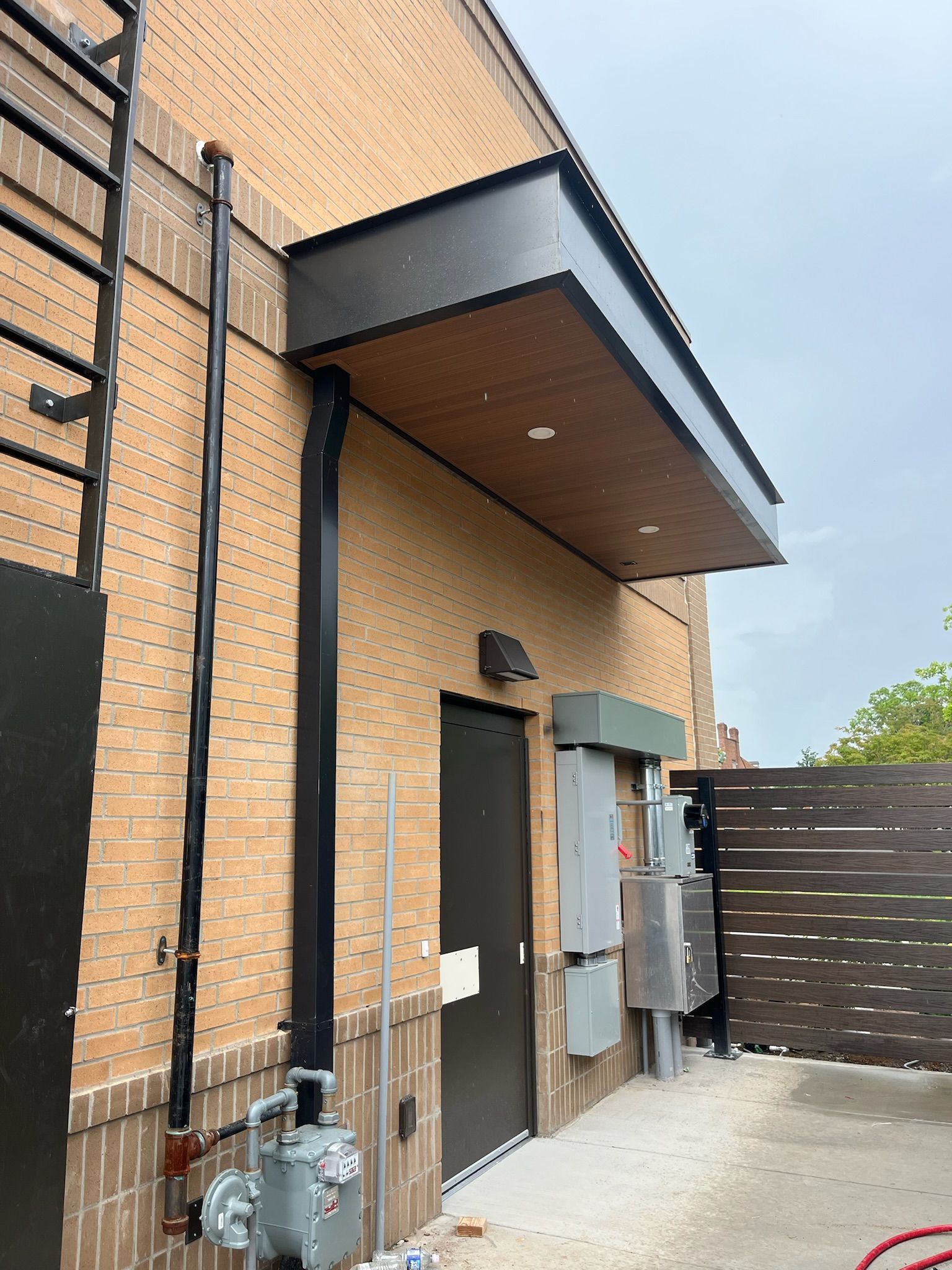 Exterior view of a brick building with a black door, awning, and utility meters.