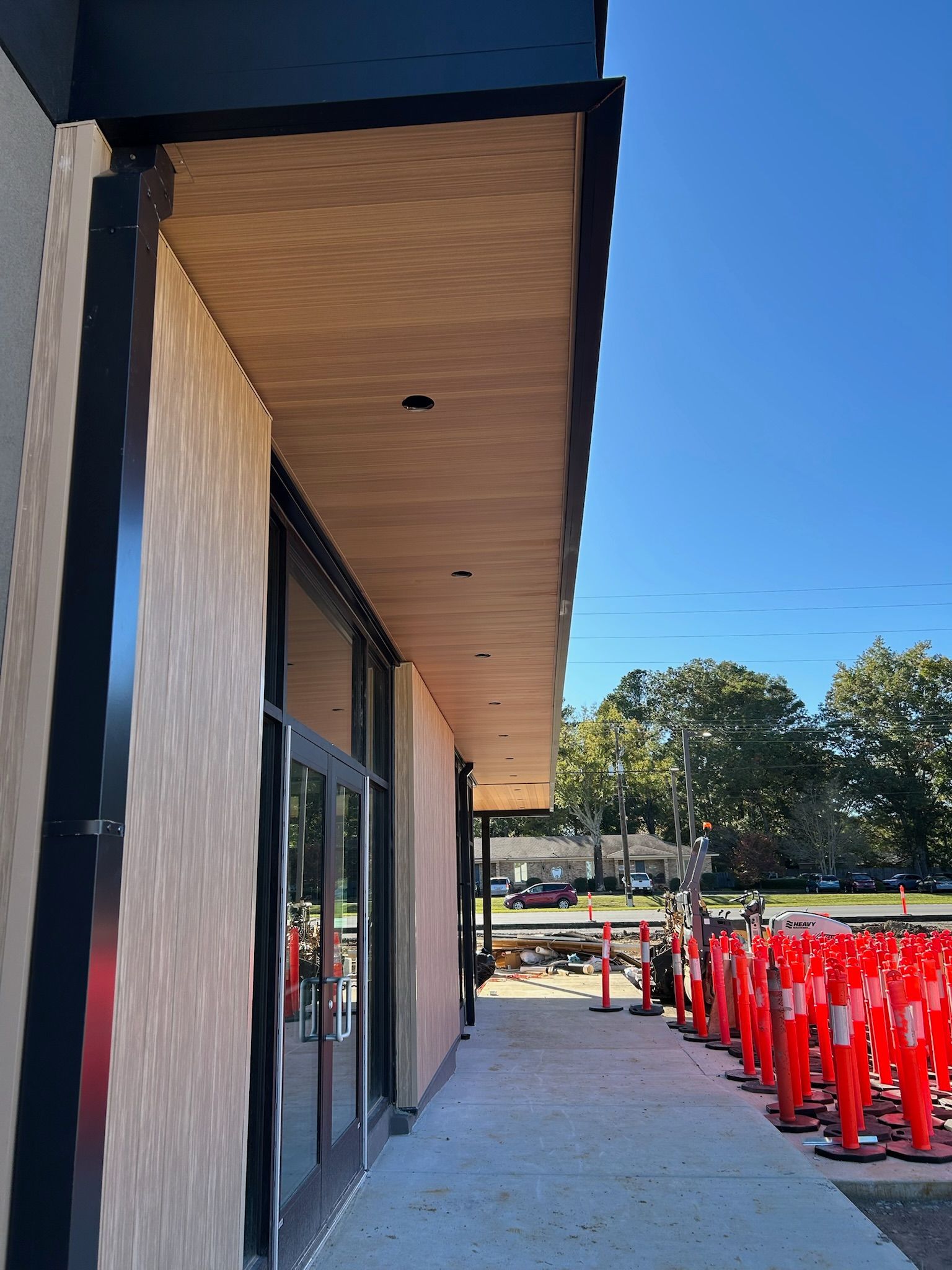 Exterior of a building with glass doors, tan stucco wall, and orange traffic cones. Blue sky overhead.