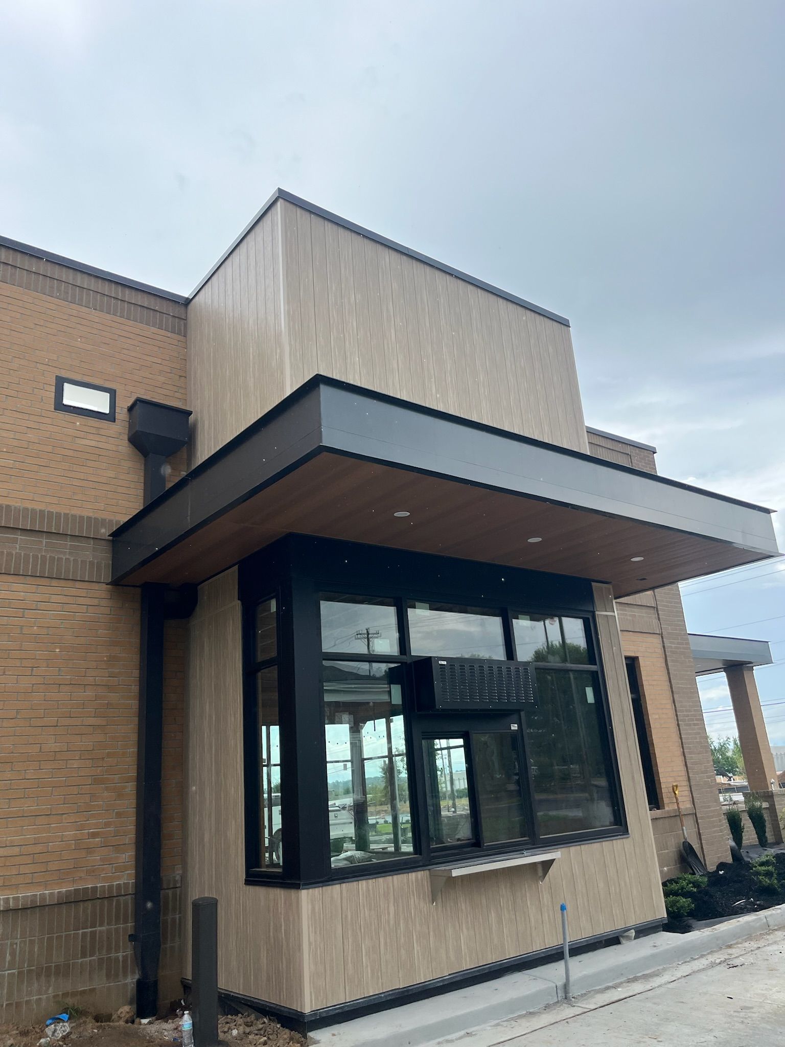 Drive-thru window of a tan-colored building with black trim, under a cloudy sky.