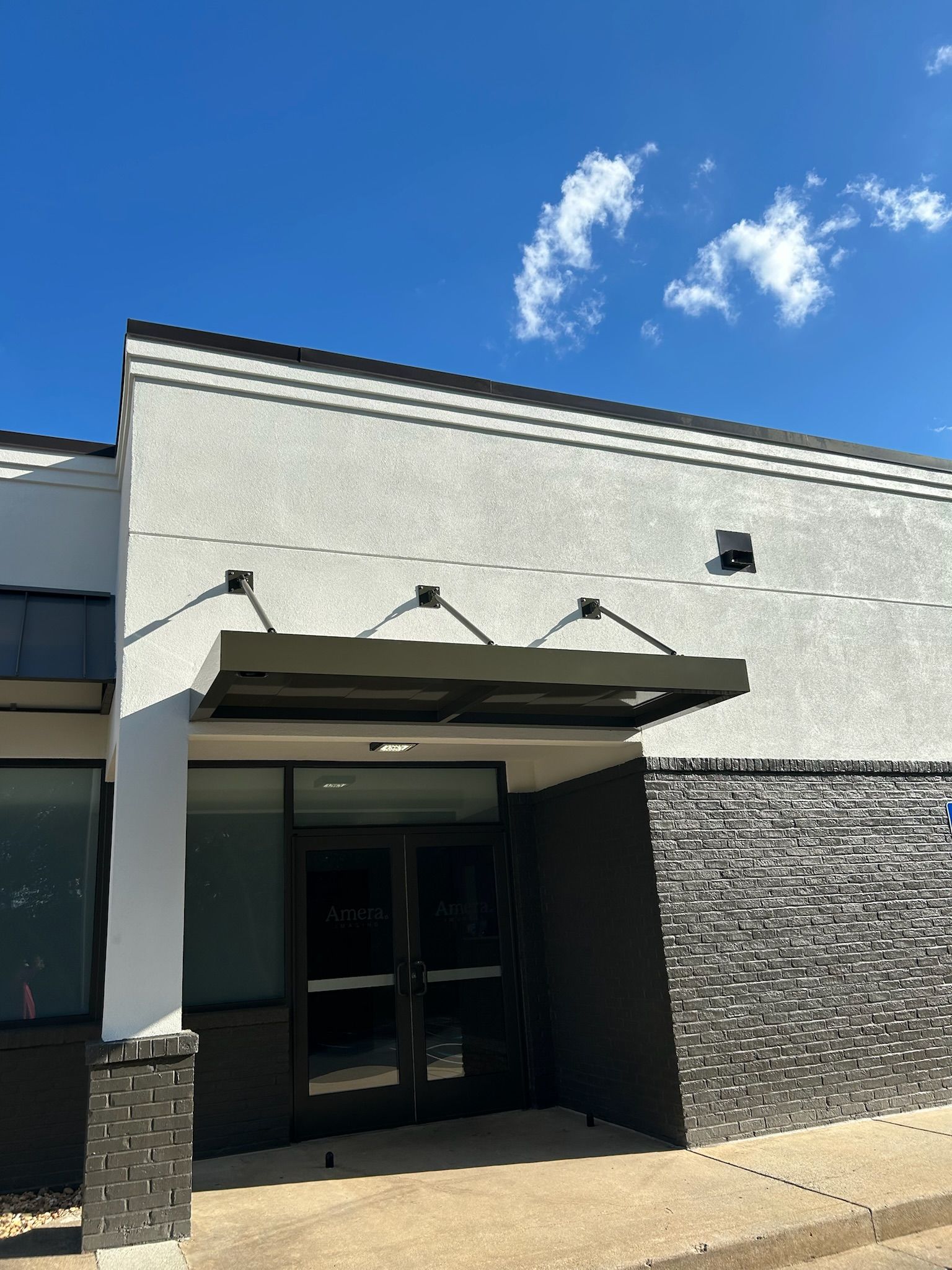 Exterior of a building with a black awning and door under a bright blue sky.