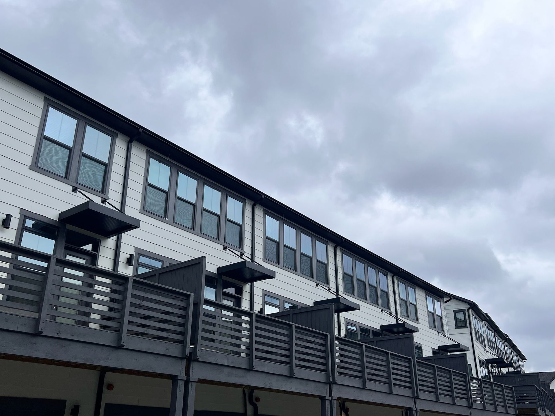 Row of modern townhouses with white siding and gray balconies under a cloudy sky.