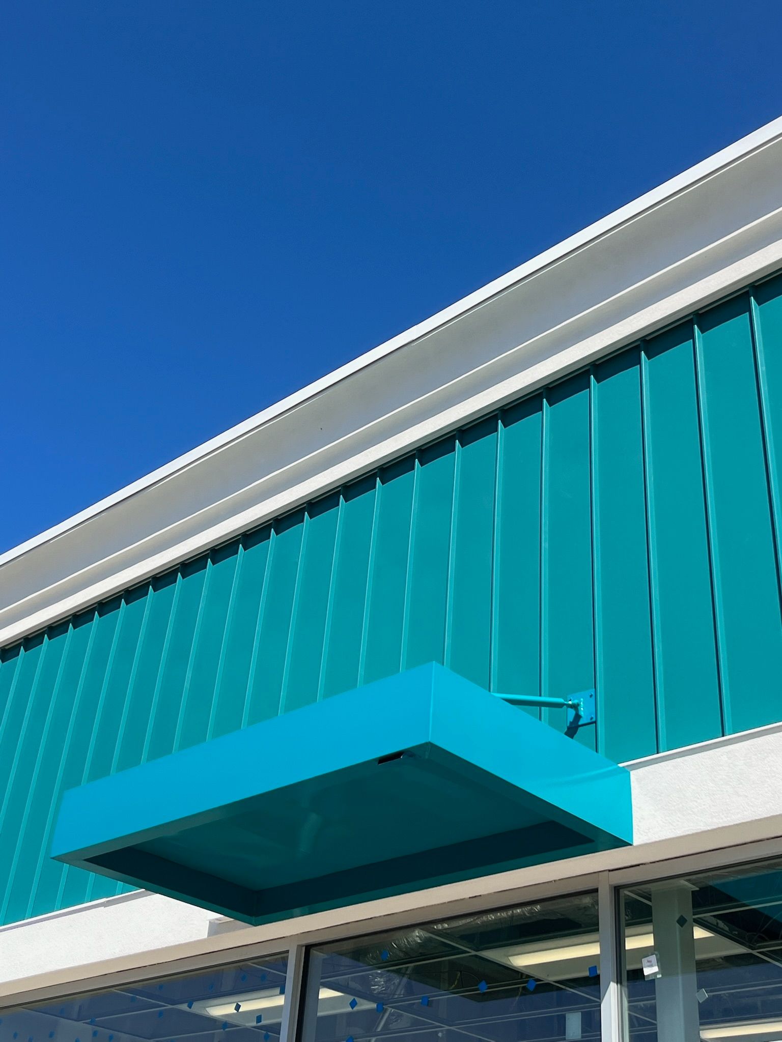 Teal and white building facade against a clear blue sky. A turquoise awning hangs above a window.