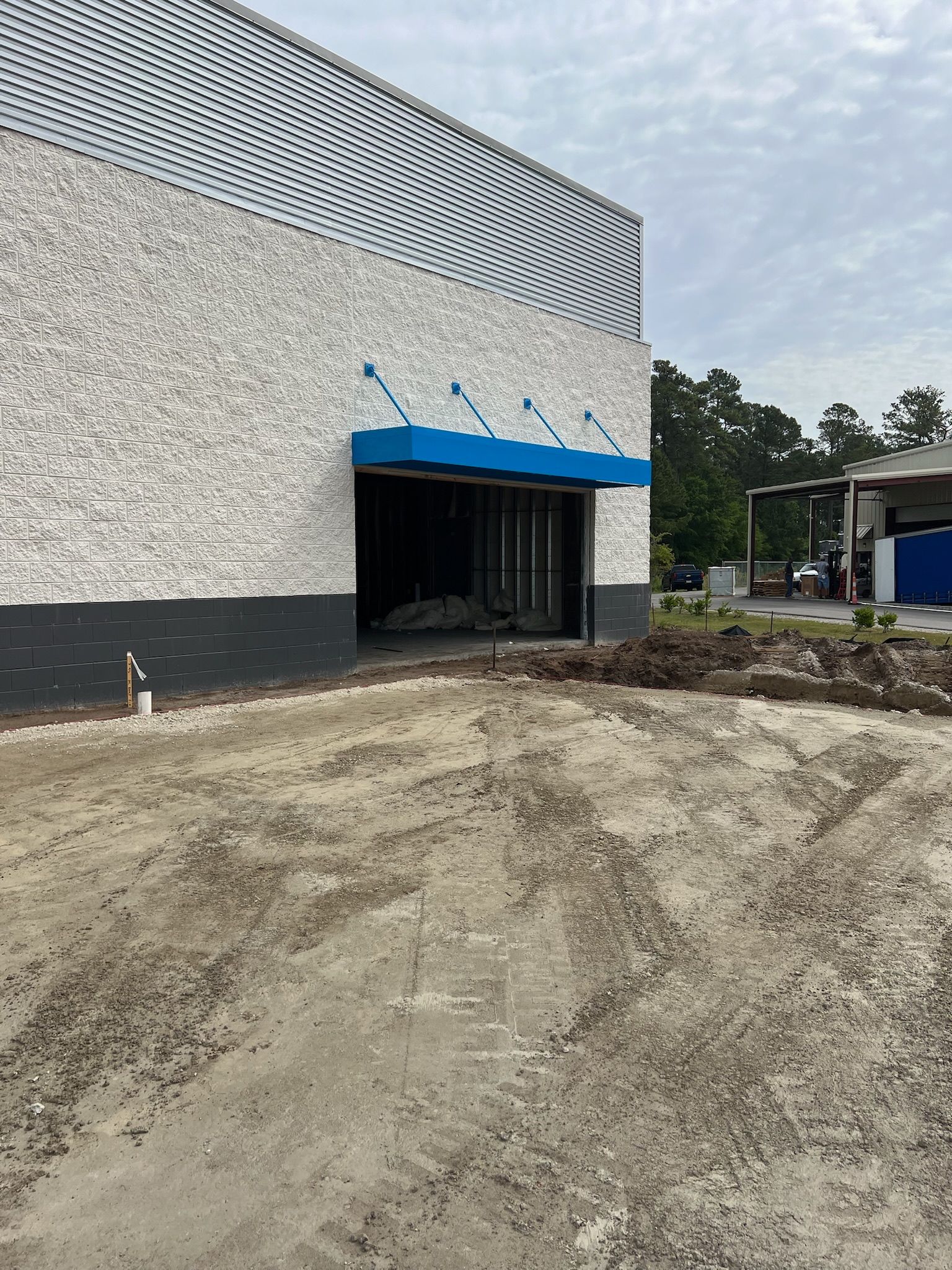 Exterior of a building under construction, featuring a brick facade with a blue awning. Gravel and dirt in foreground.