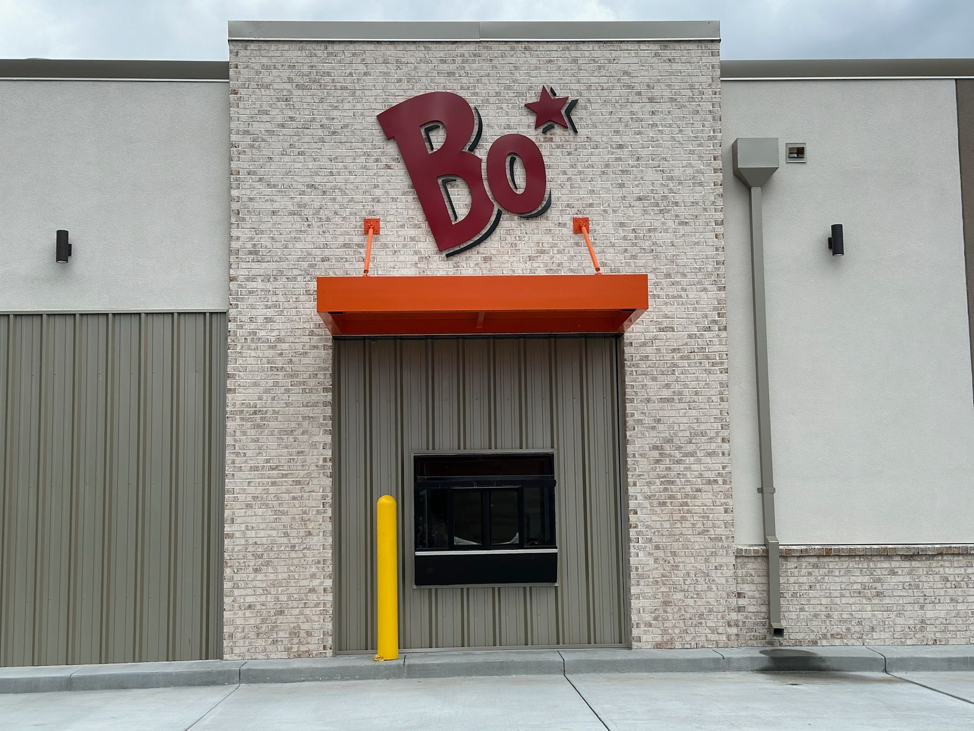 Bojangles restaurant storefront with red logo above order window, orange awning, and gray/beige walls.