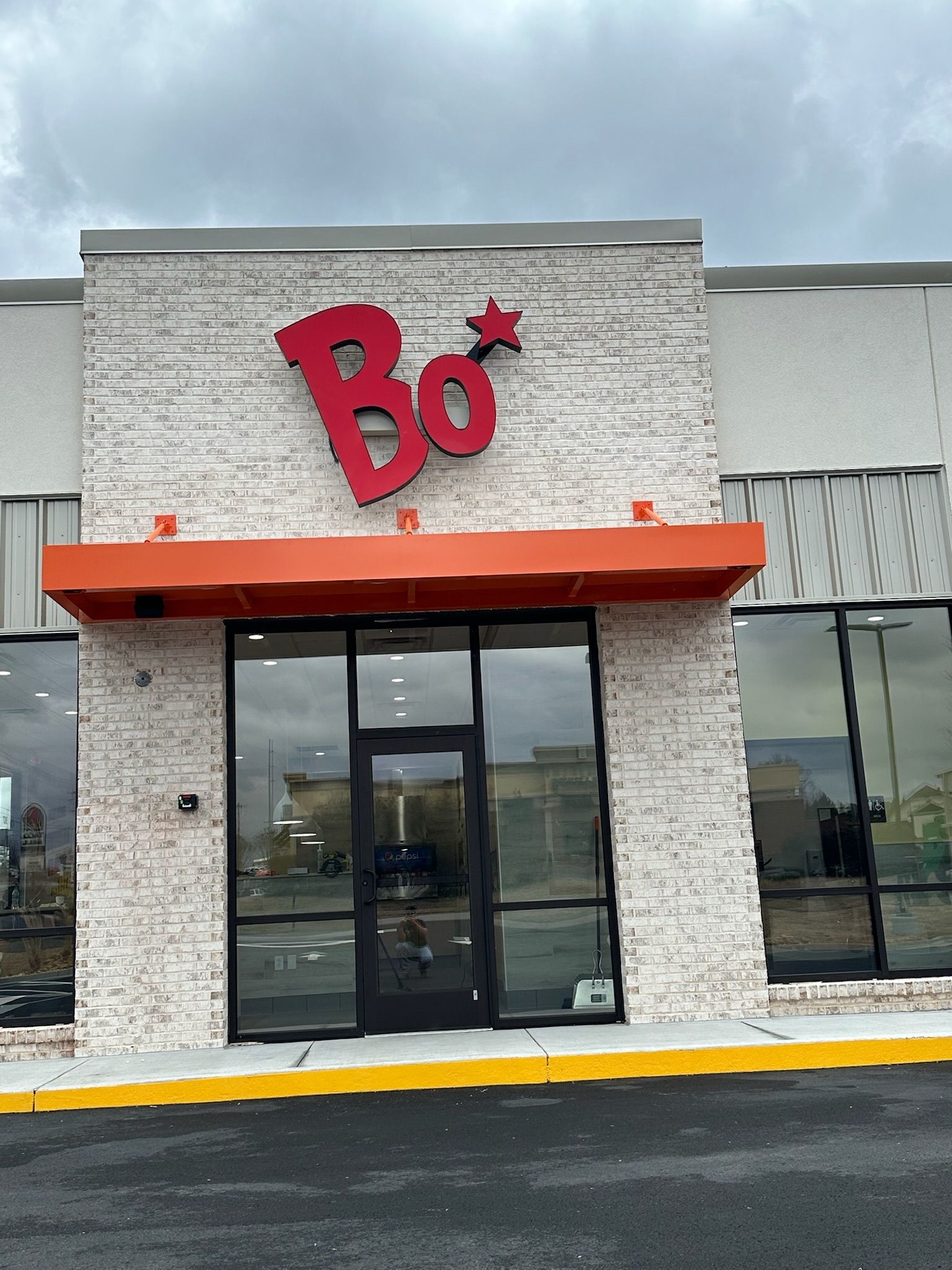 Bojangles restaurant storefront with red logo above entrance. Orange awning. Gray brick facade.
