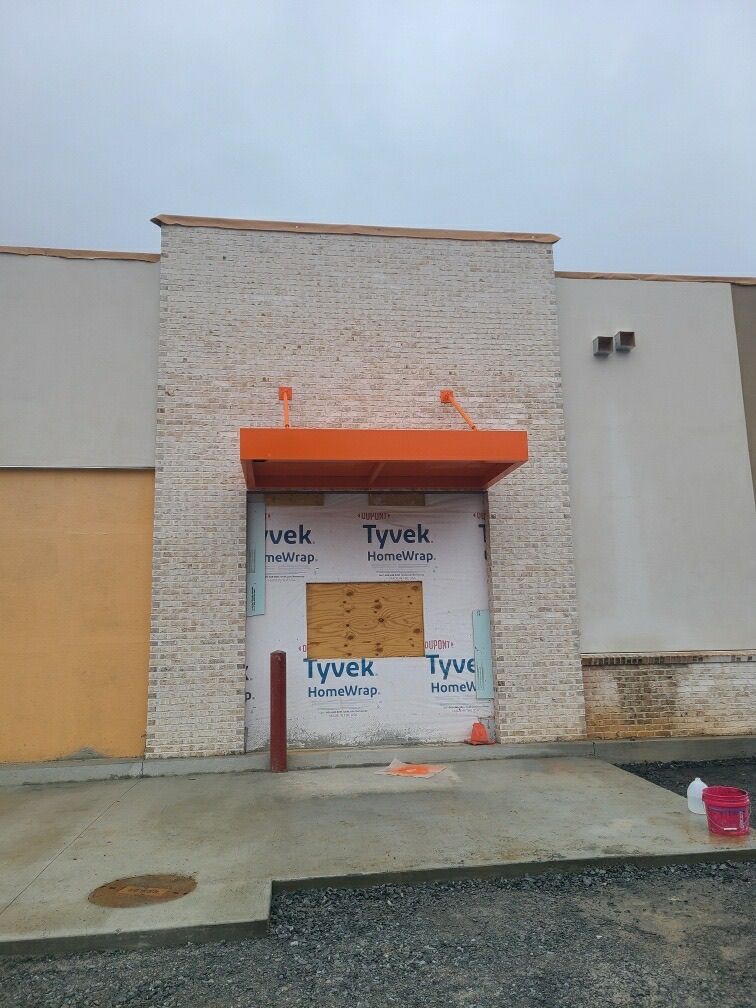 Exterior of a building with a boarded-up entrance. Orange canopy over the doorway; white brickwork.