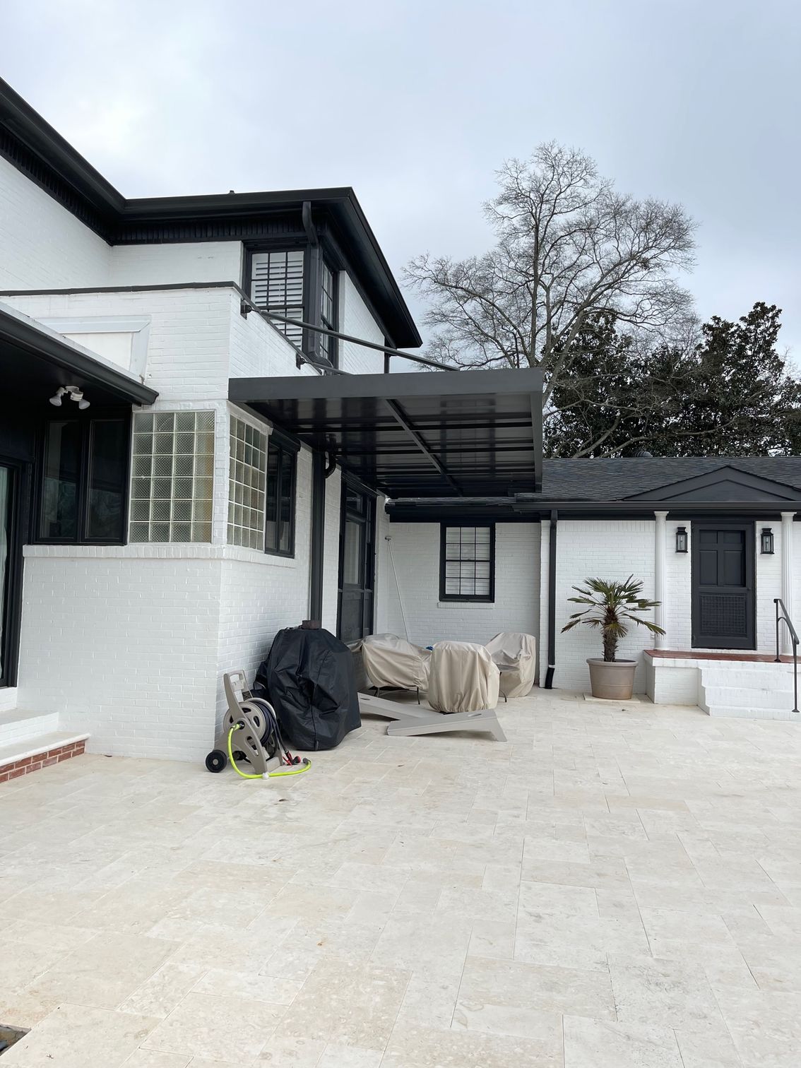 Exterior of a white brick house with black trim. A covered patio, a small side building, and a concrete patio are visible.