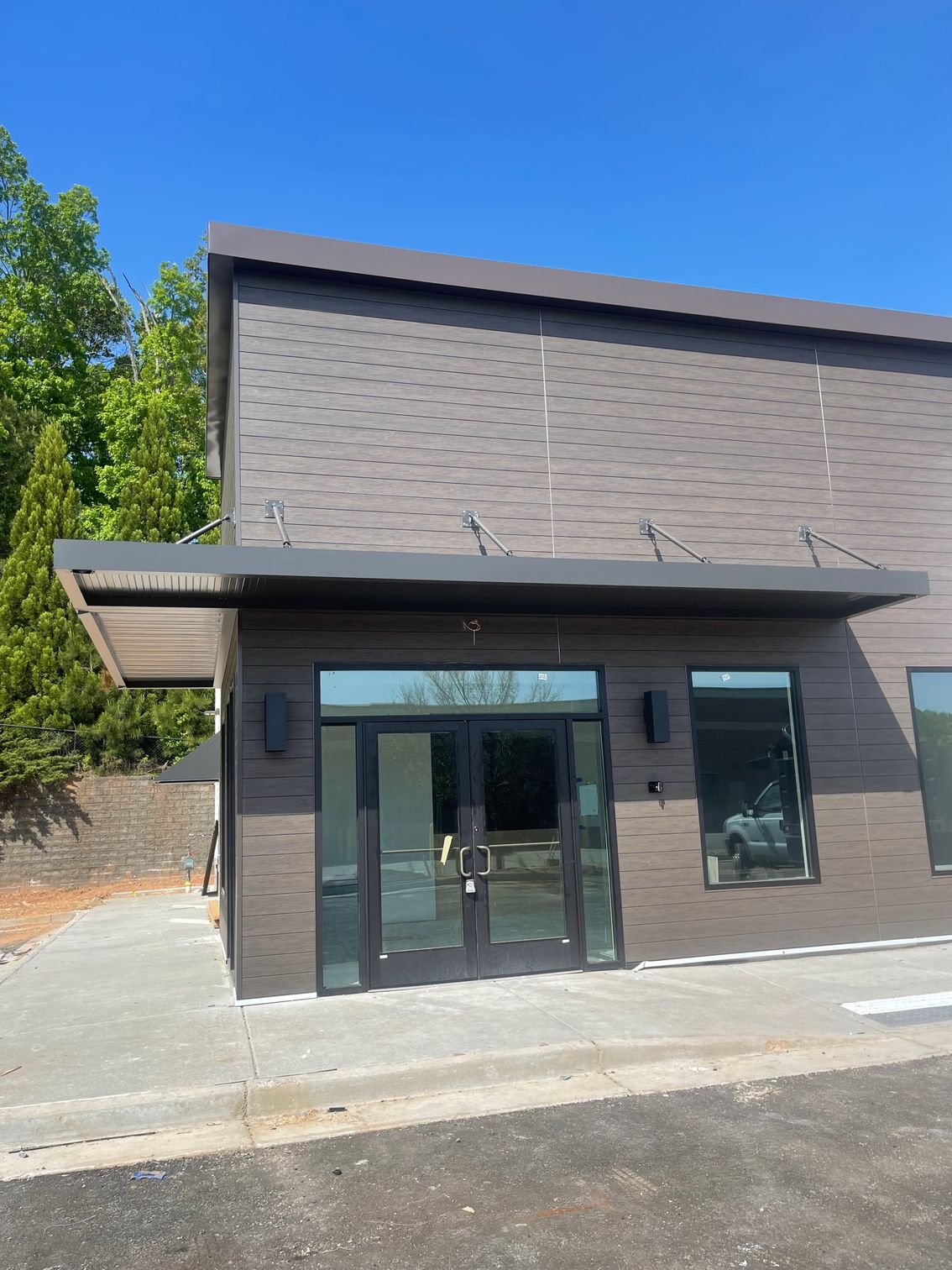 Brown building with glass doors and windows, under a dark roof, on a sunny day.