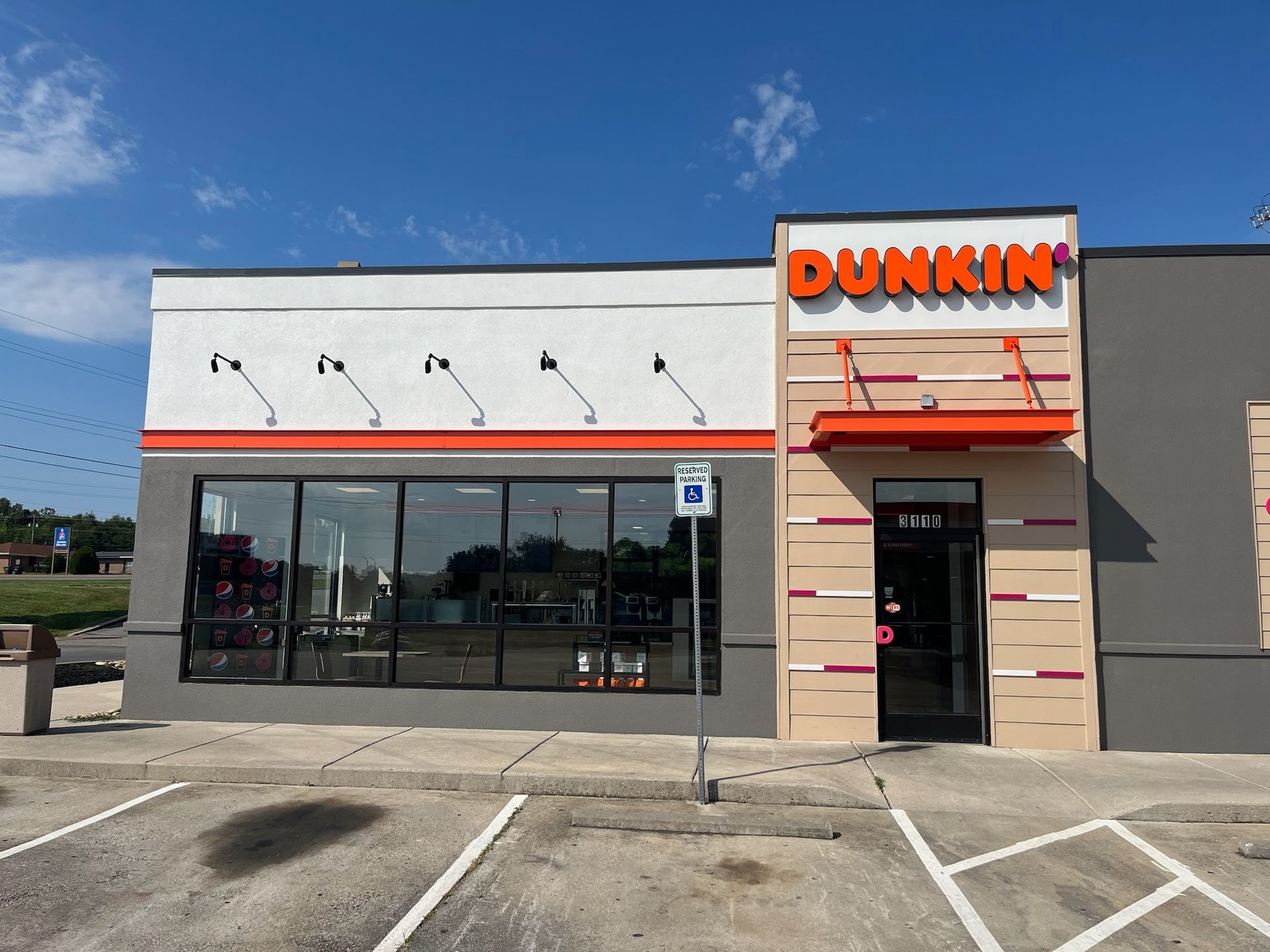 Dunkin' Donuts storefront, gray and orange facade, blue sky, accessible parking spot in front.