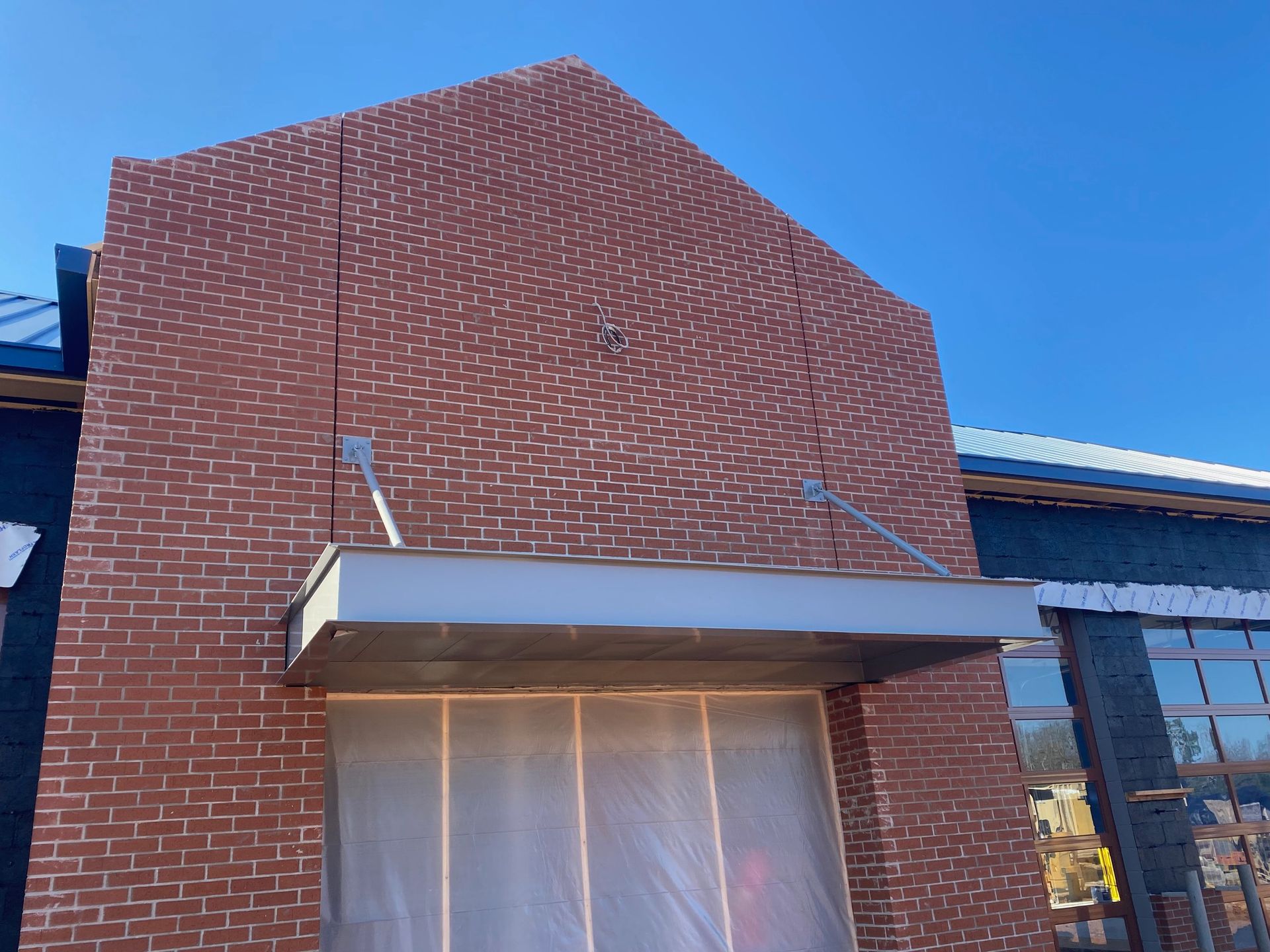 Brick building facade with a metal awning over a doorway covered in plastic; blue sky.