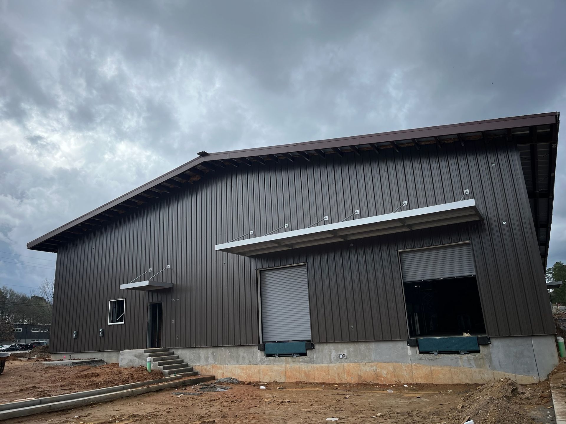 Dark brown metal building with a loading dock under a cloudy sky.