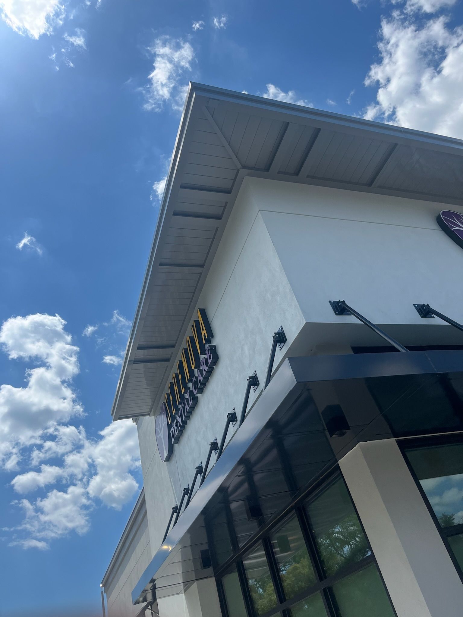 White building corner with black trim, sign, and clear blue sky with clouds.